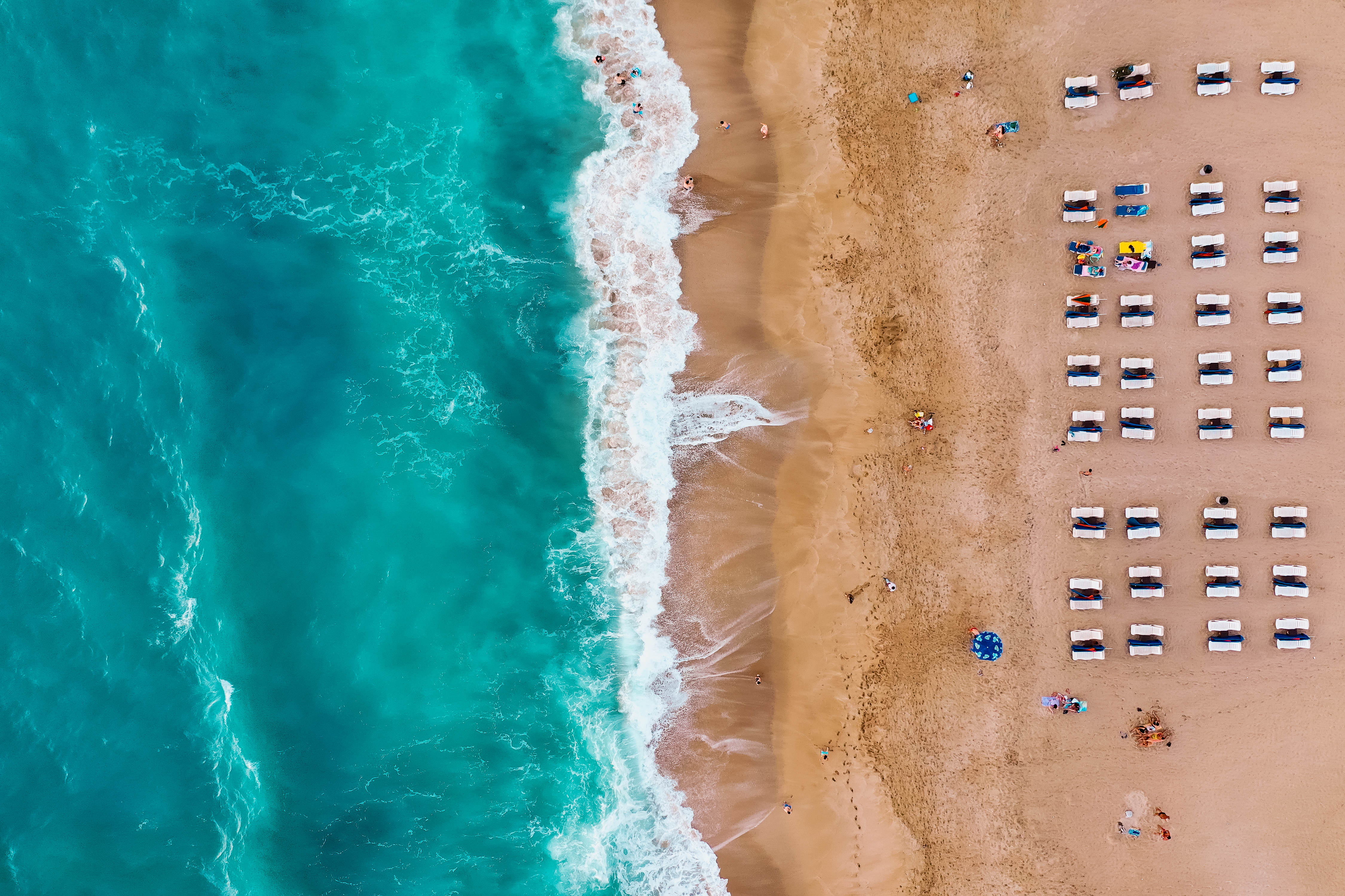 Aerial view: tropical sandy beach, turquoise ocean waves, sun loungers.