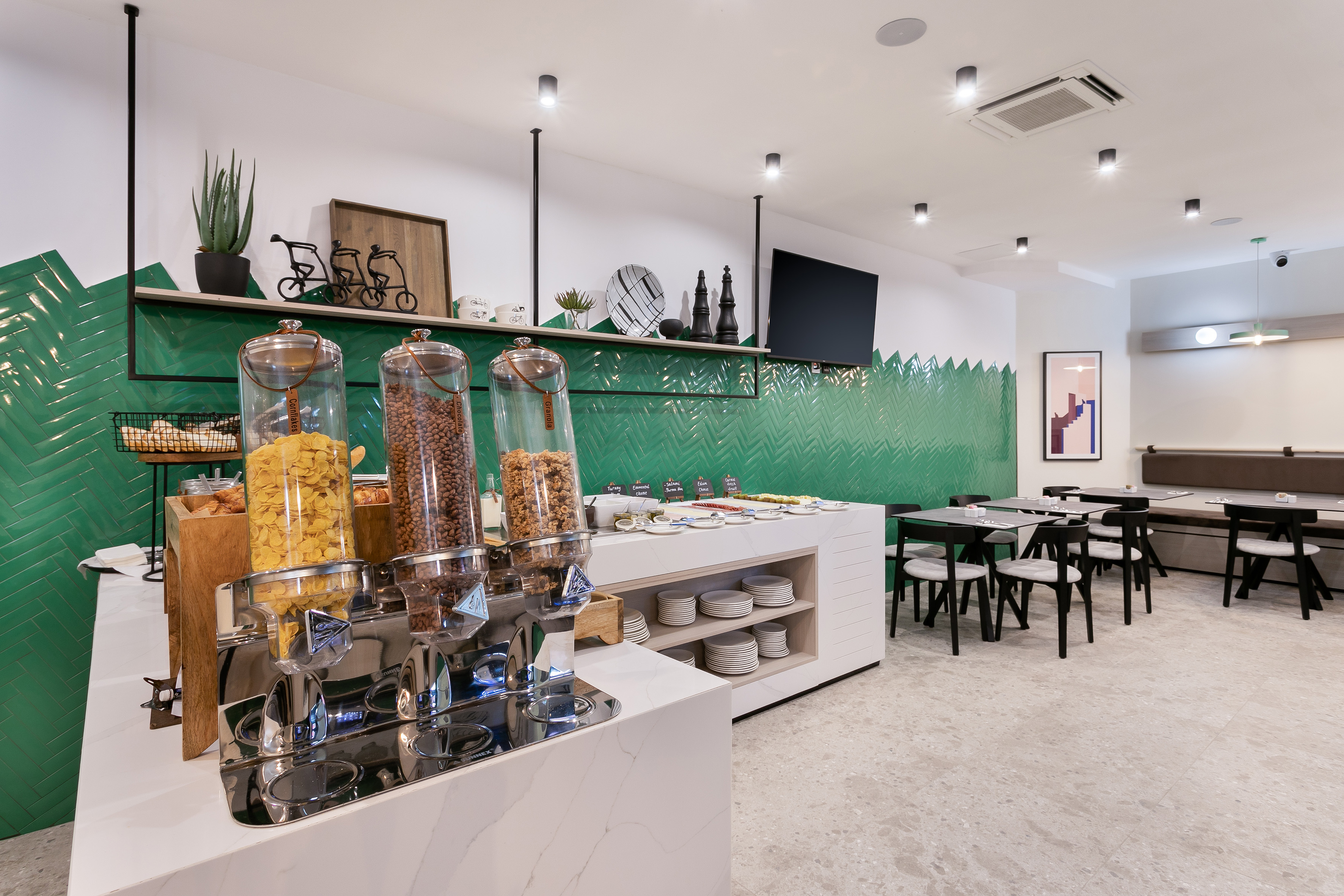 Modern breakfast buffet with cereal dispensers and green tiled wall.
