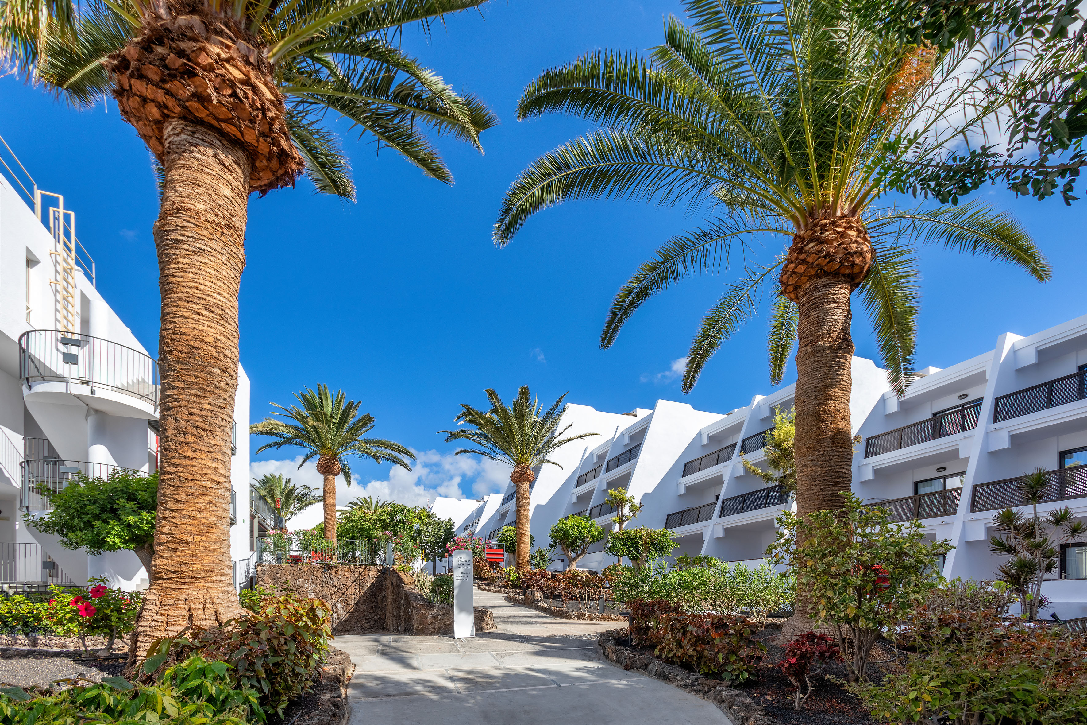 Tropical resort hotel with white architecture, palm trees, and blue sky.