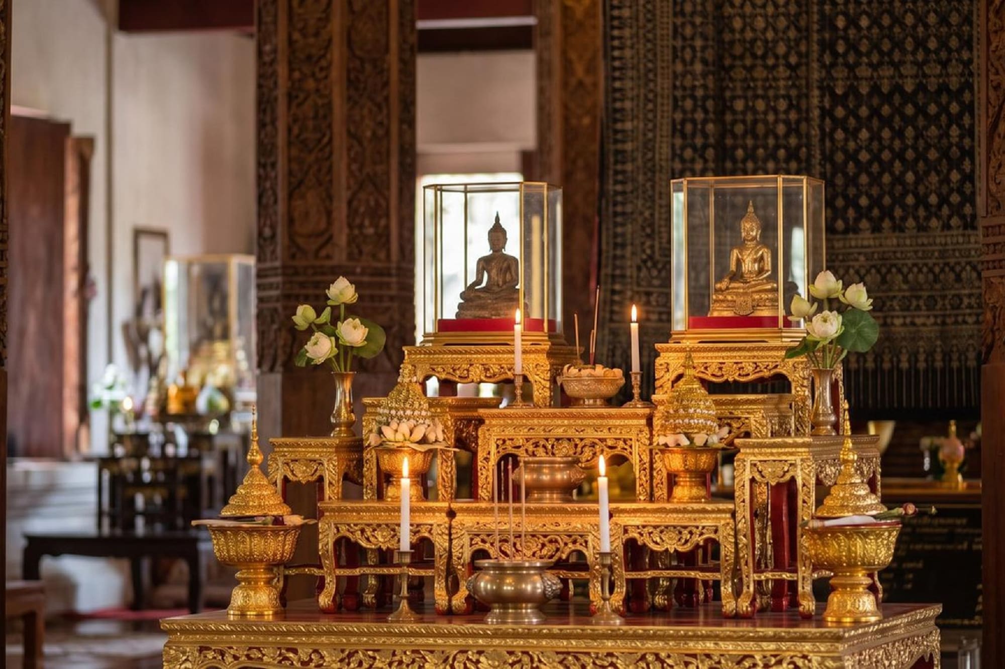 Ornate golden Buddhist altar with Buddha statues, lit candles, and lotus flowers.