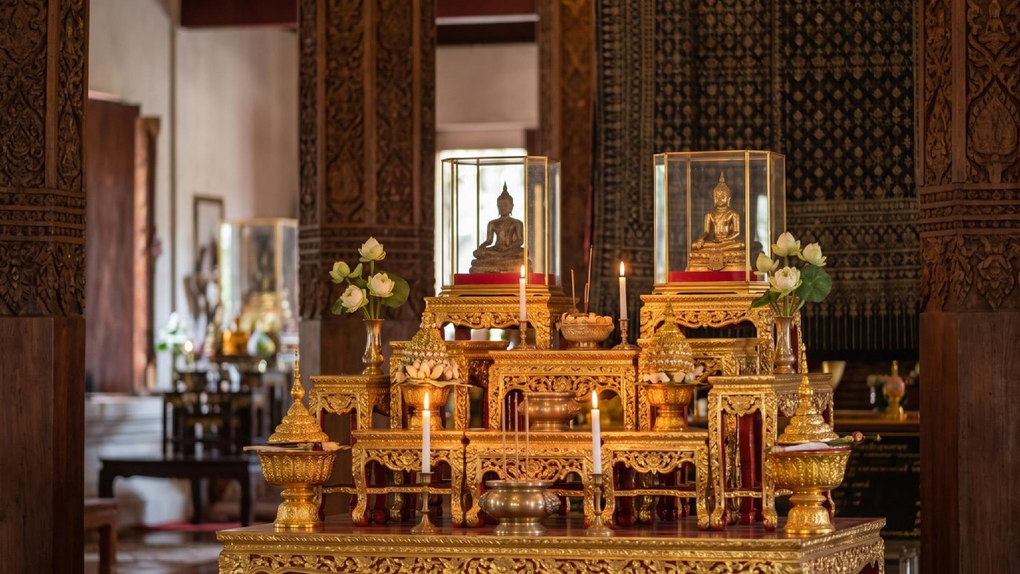 Ornate golden Buddhist altar with Buddha statues, lit candles, and lotus flowers.