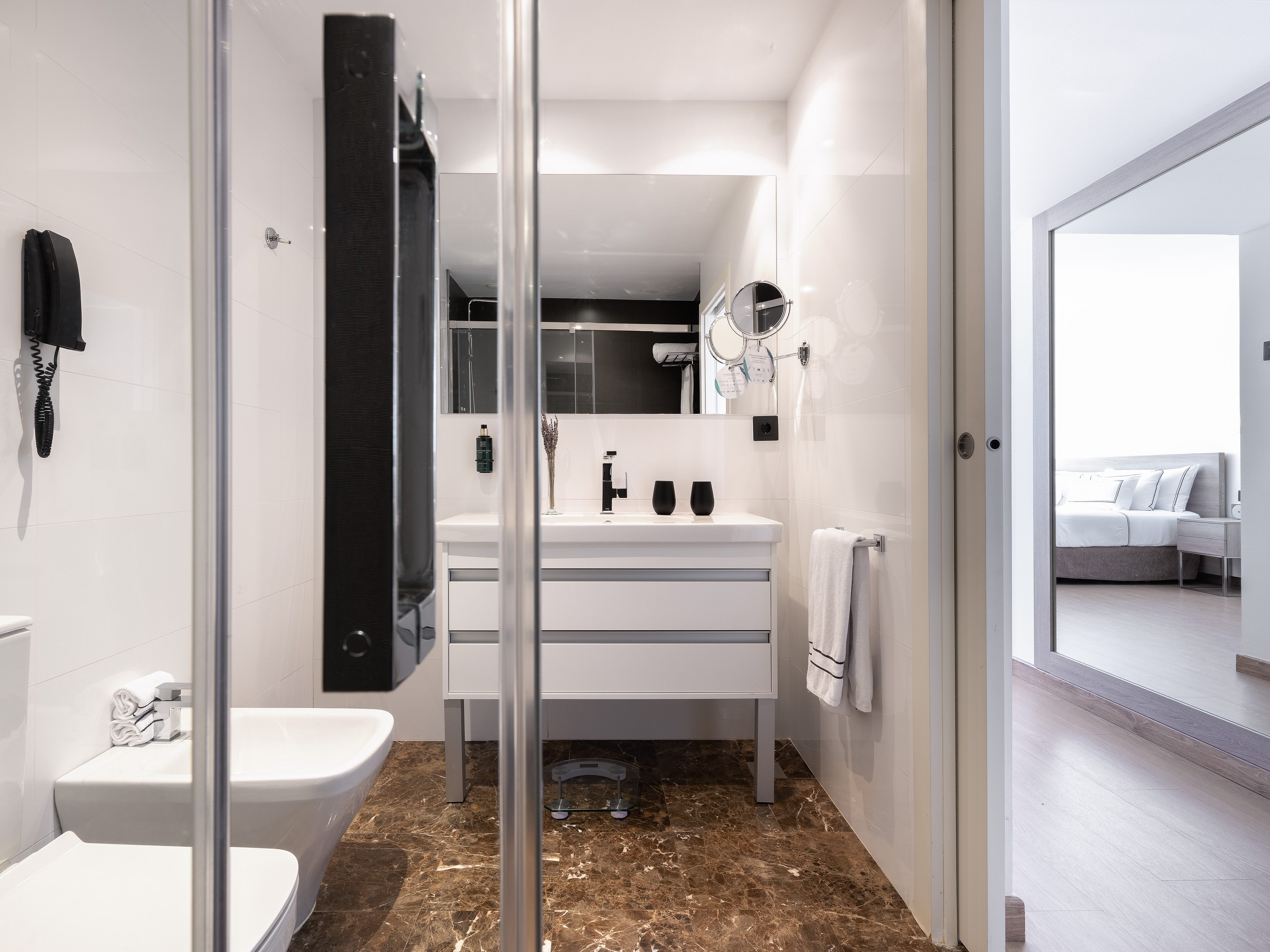 Modern bathroom with white vanity, brown marble floor, glass shower, and toilet.