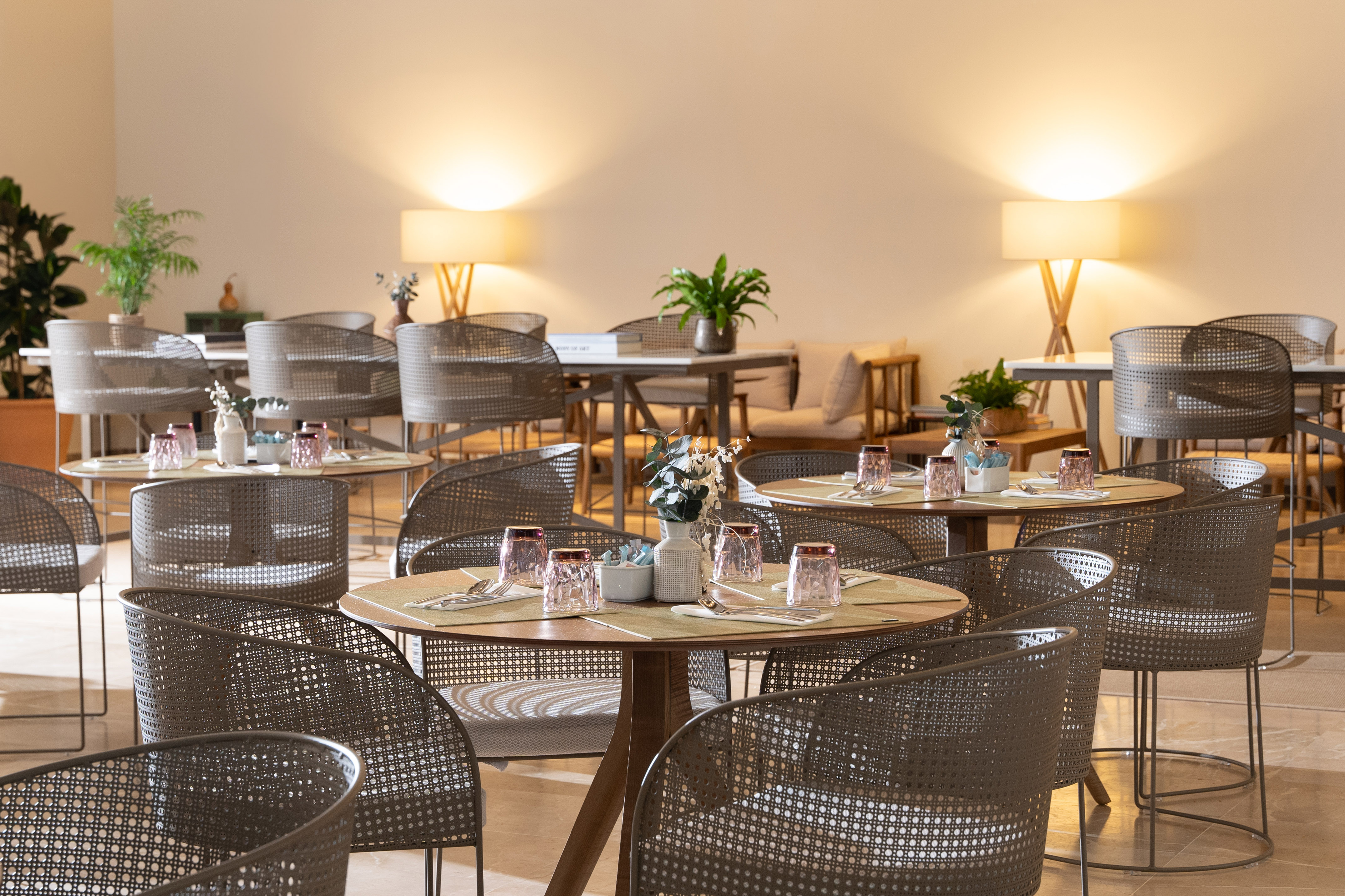 Restaurant dining area with set round tables, perforated chairs, and warm lighting.