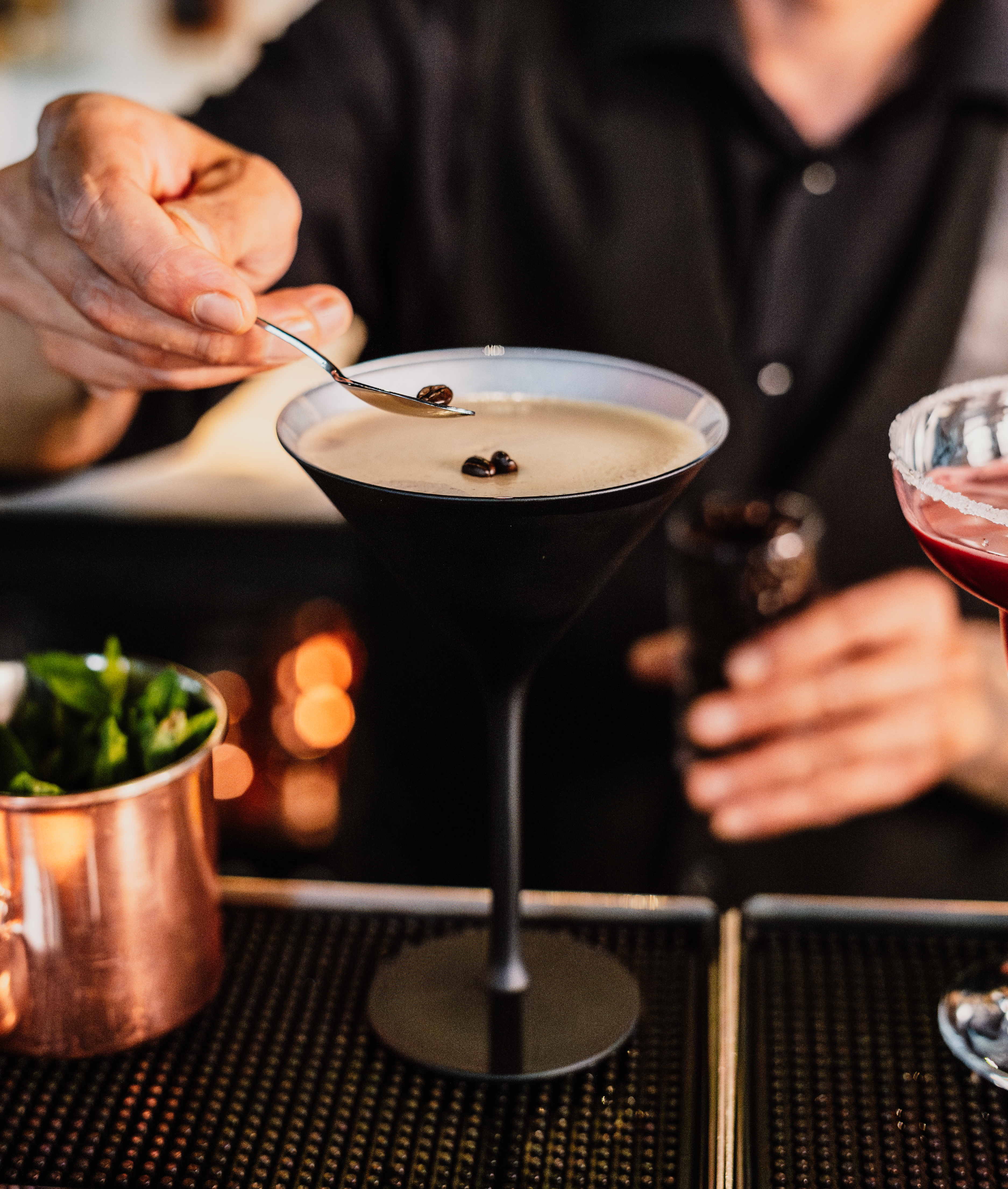 Bartender garnishing an Espresso Martini with coffee beans at a bar.