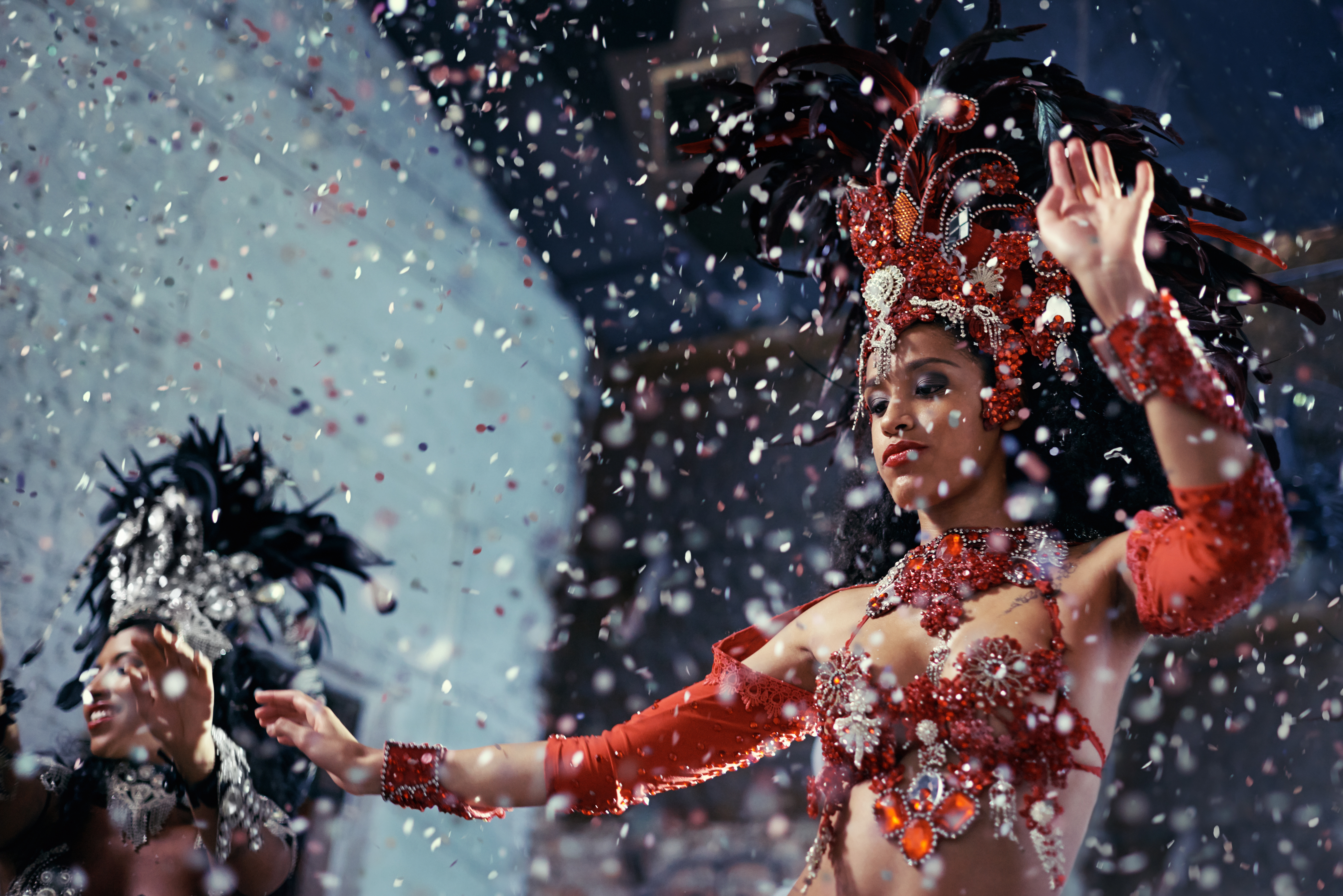 Samba dancer in elaborate red feathered costume with falling confetti.