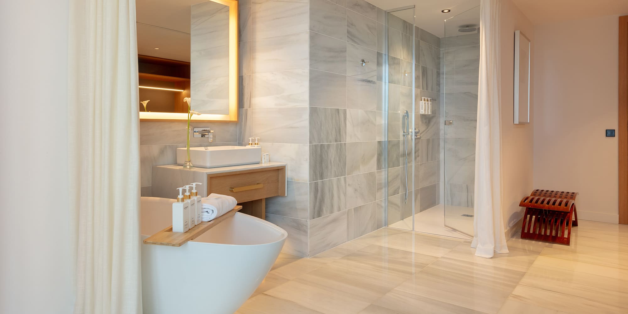 Luxury bathroom with freestanding tub, marble walk-in shower, and illuminated mirror.