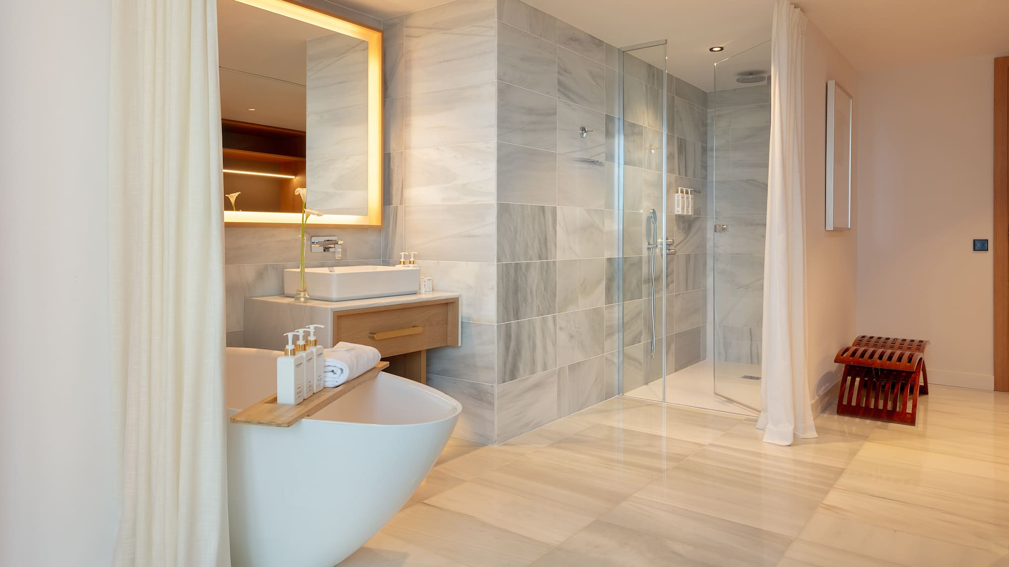 Luxury bathroom with freestanding tub, marble walk-in shower, and illuminated mirror.