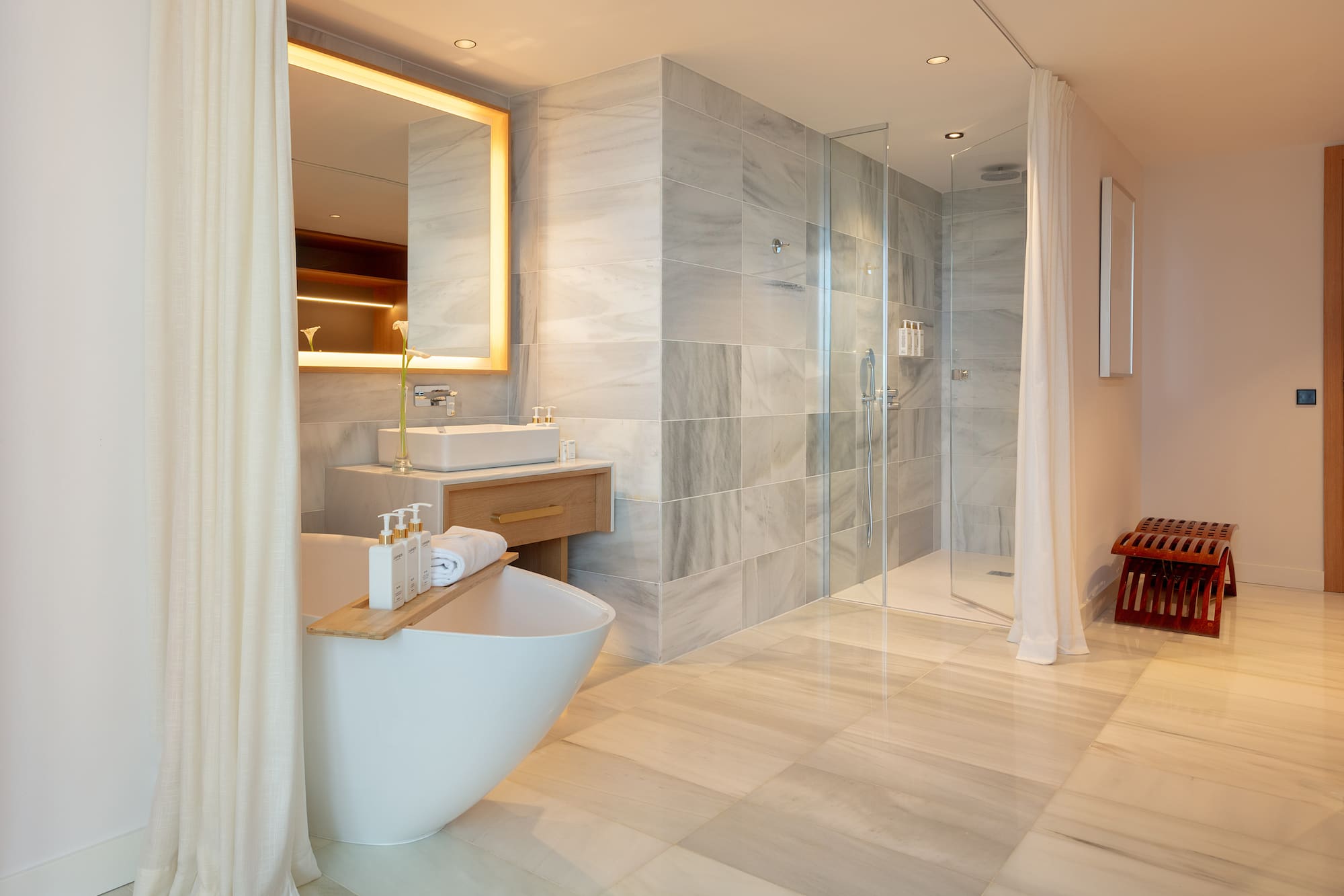 Luxury bathroom with freestanding tub, marble walk-in shower, and illuminated mirror.