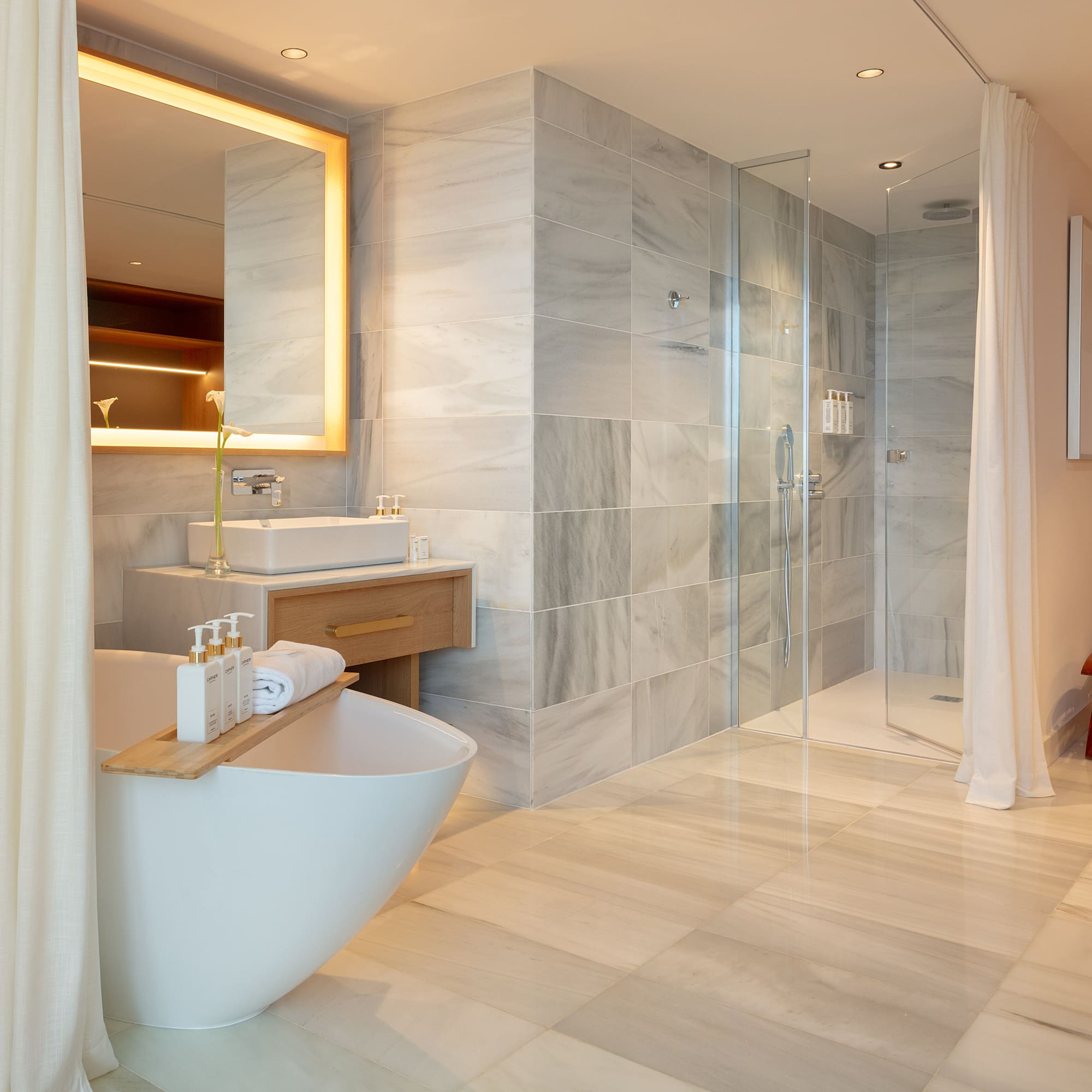 Luxury bathroom with freestanding tub, marble walk-in shower, and illuminated mirror.