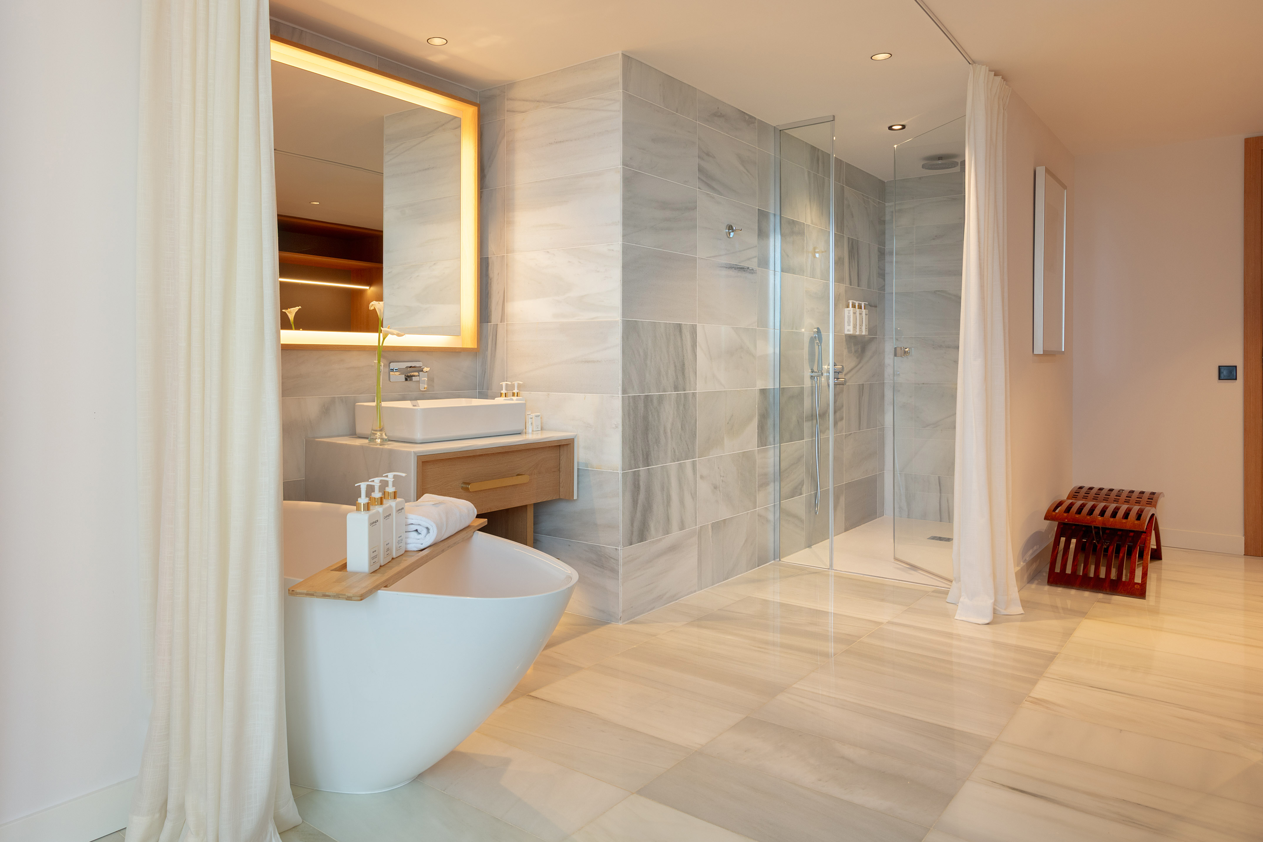 Luxury bathroom with freestanding tub, marble walk-in shower, and illuminated mirror.