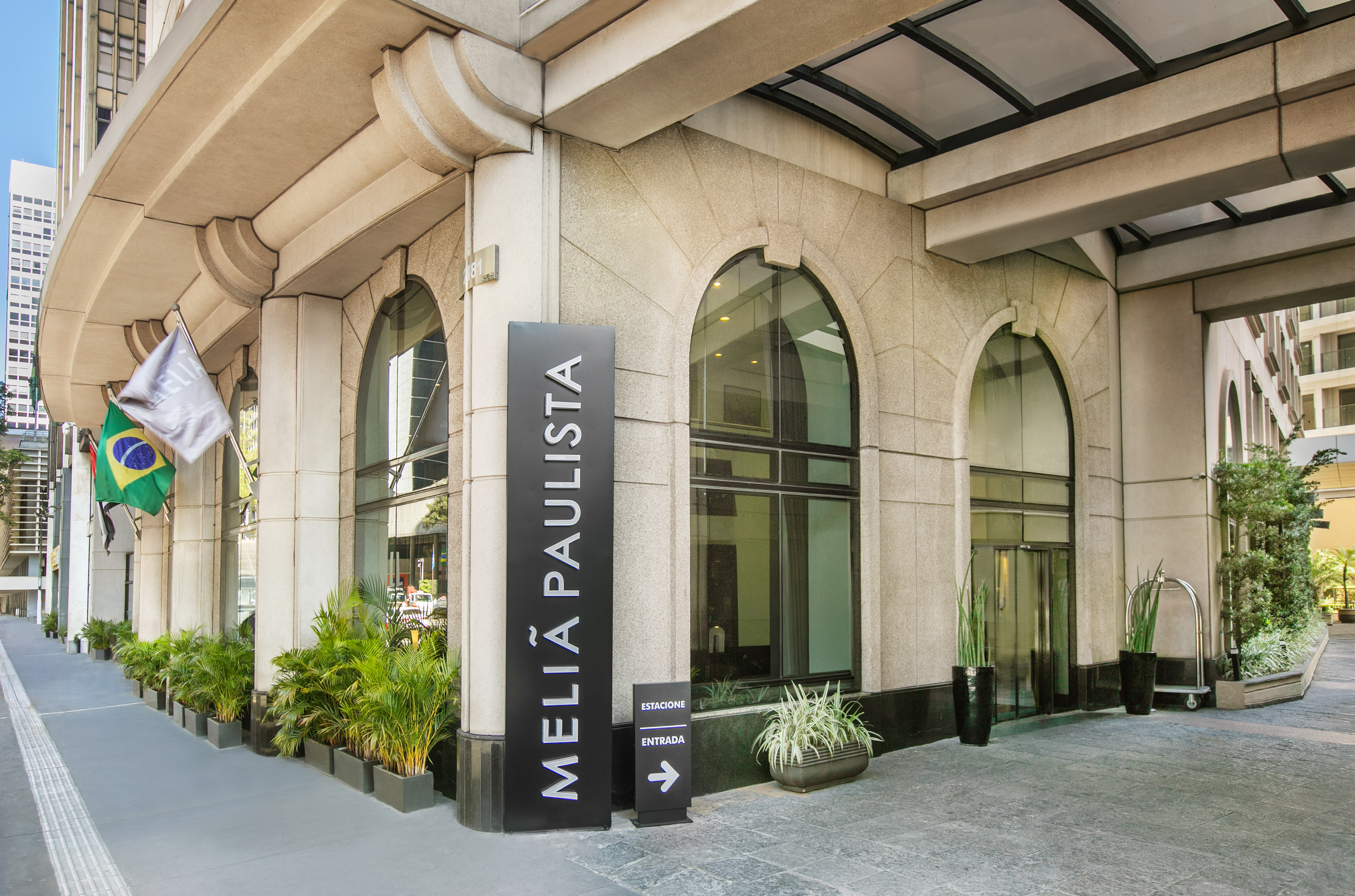 Meliá Paulista hotel entrance with arched windows, stone facade, and Brazilian flag.