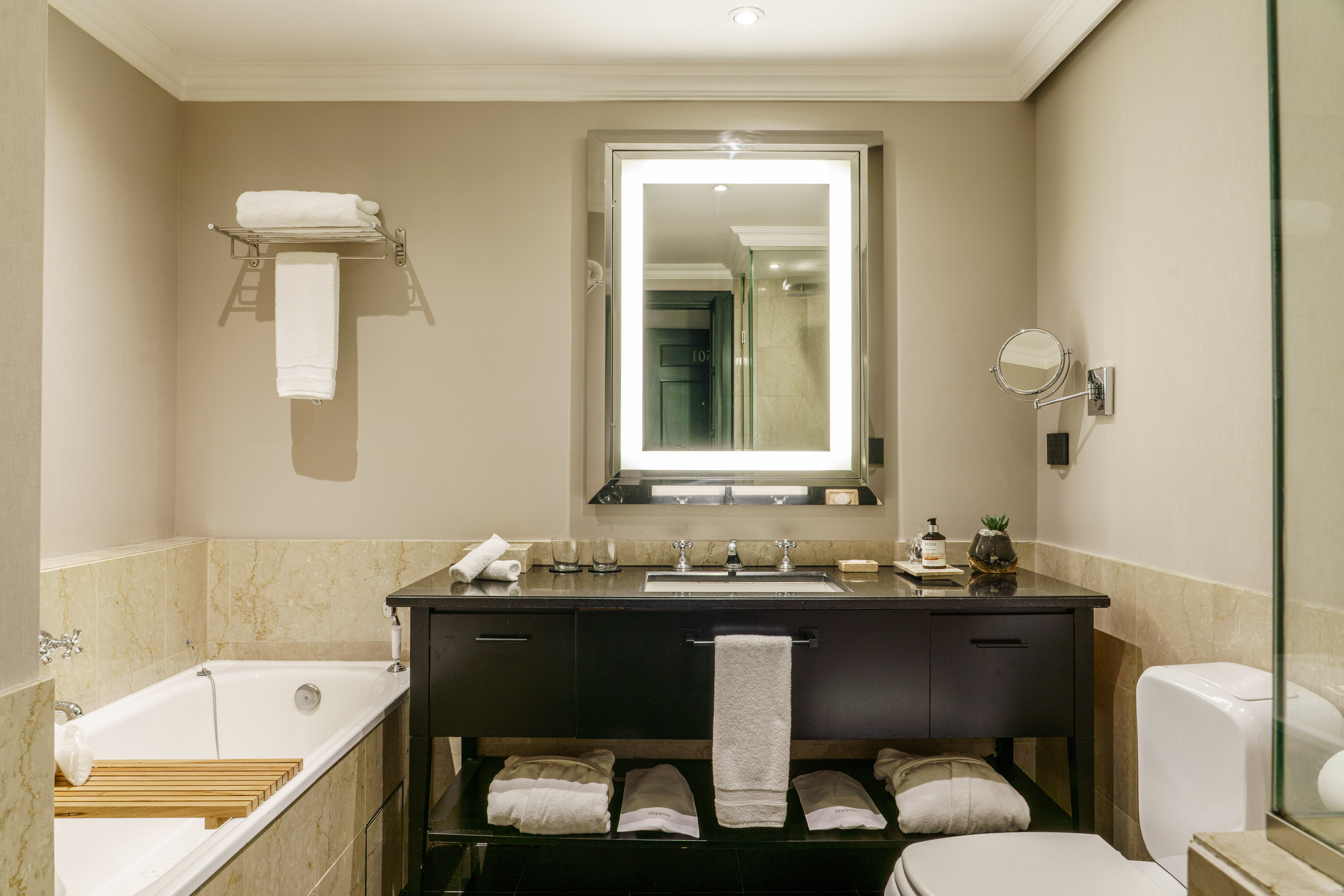Luxury hotel bathroom with bathtub, dark vanity, and illuminated mirror.