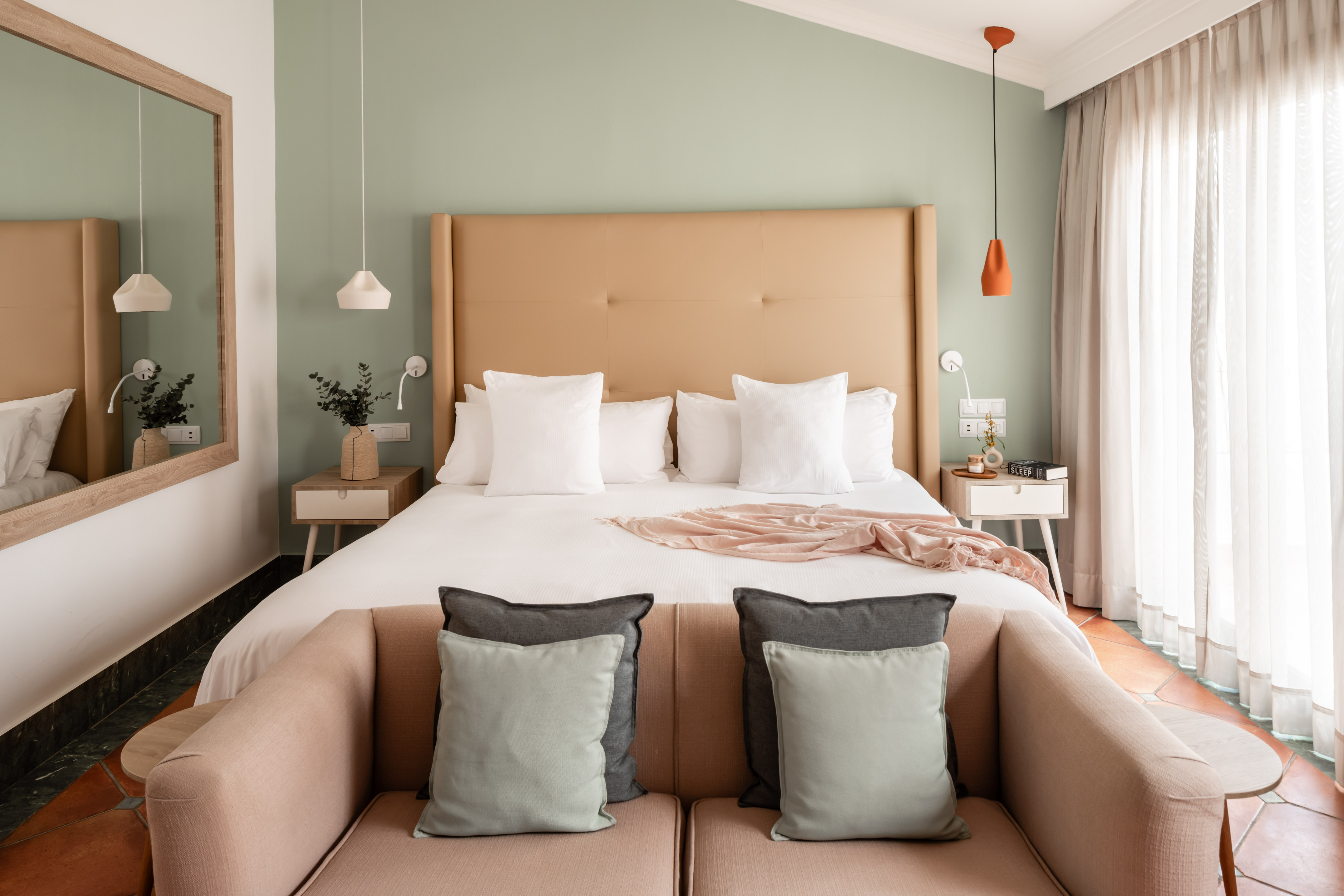 Cozy bedroom with tan headboard, white bedding, sage green walls, and sofa.