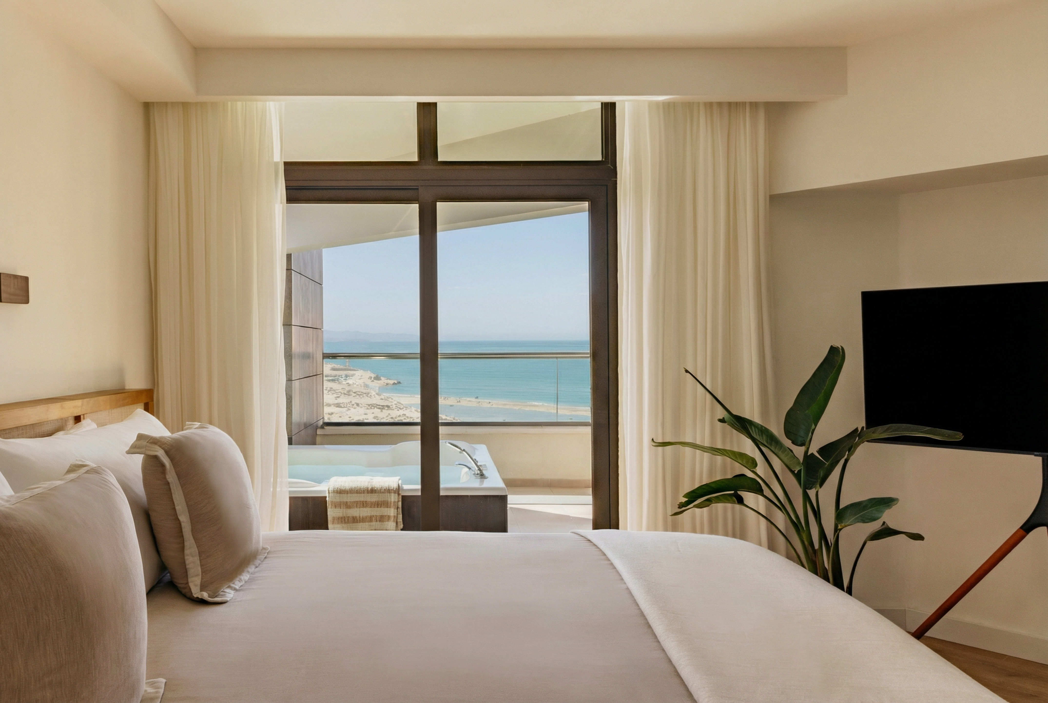 Modern hotel bedroom with ocean view and balcony jacuzzi.