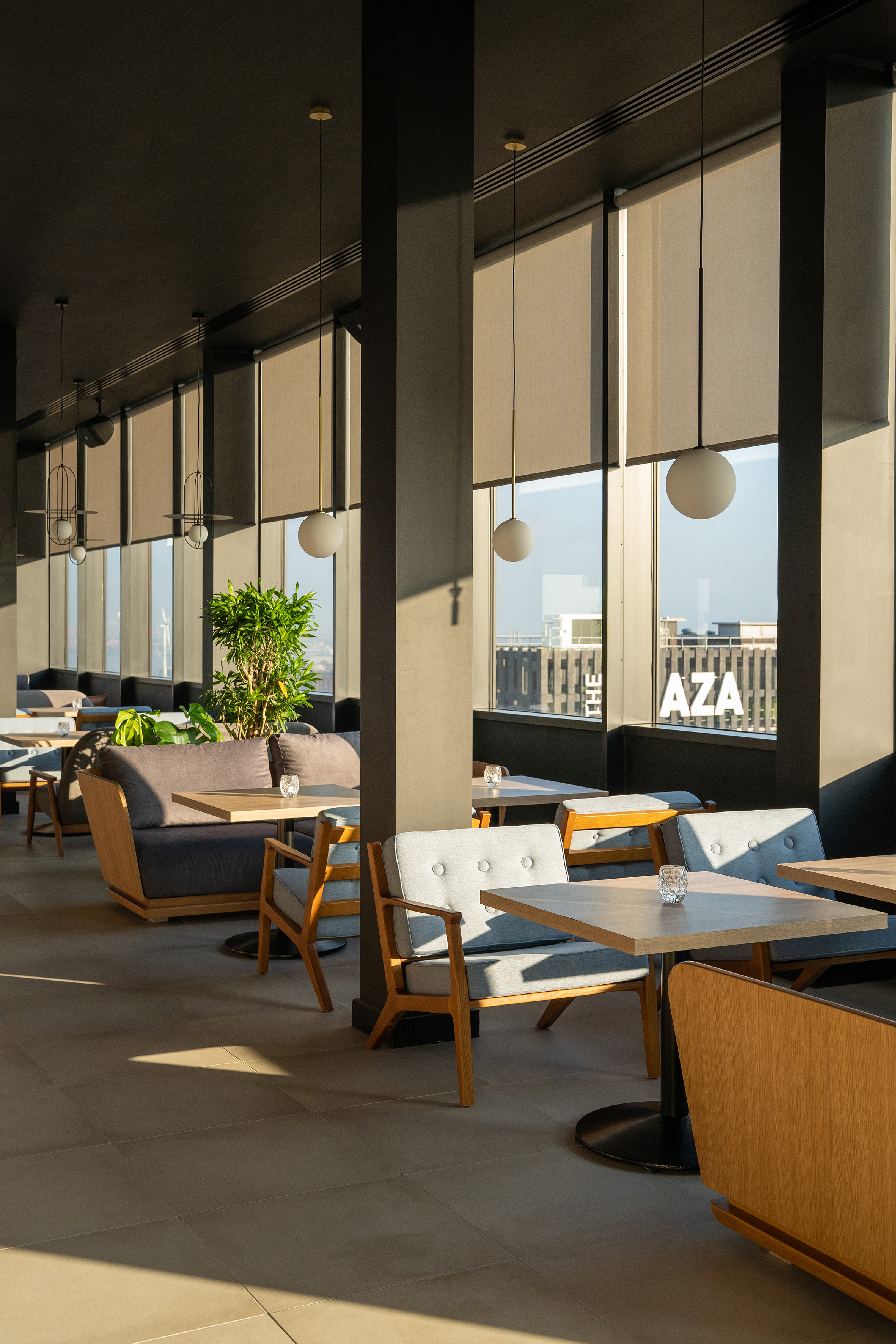 Modern cafe interior with wooden furniture, gray seating, and sunny city view.