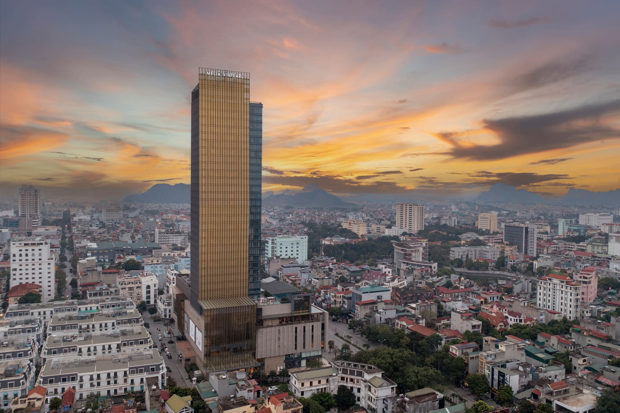 Golden Melia Vinpearl skyscraper, city panorama at sunset, distant mountains.