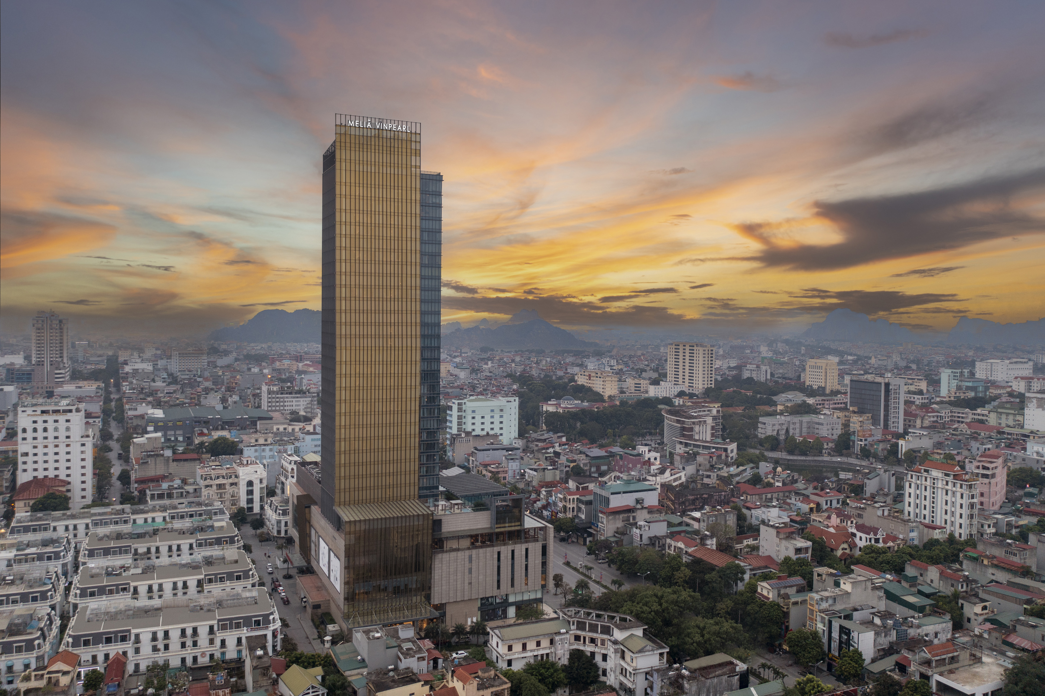Golden Melia Vinpearl skyscraper, city panorama at sunset, distant mountains.