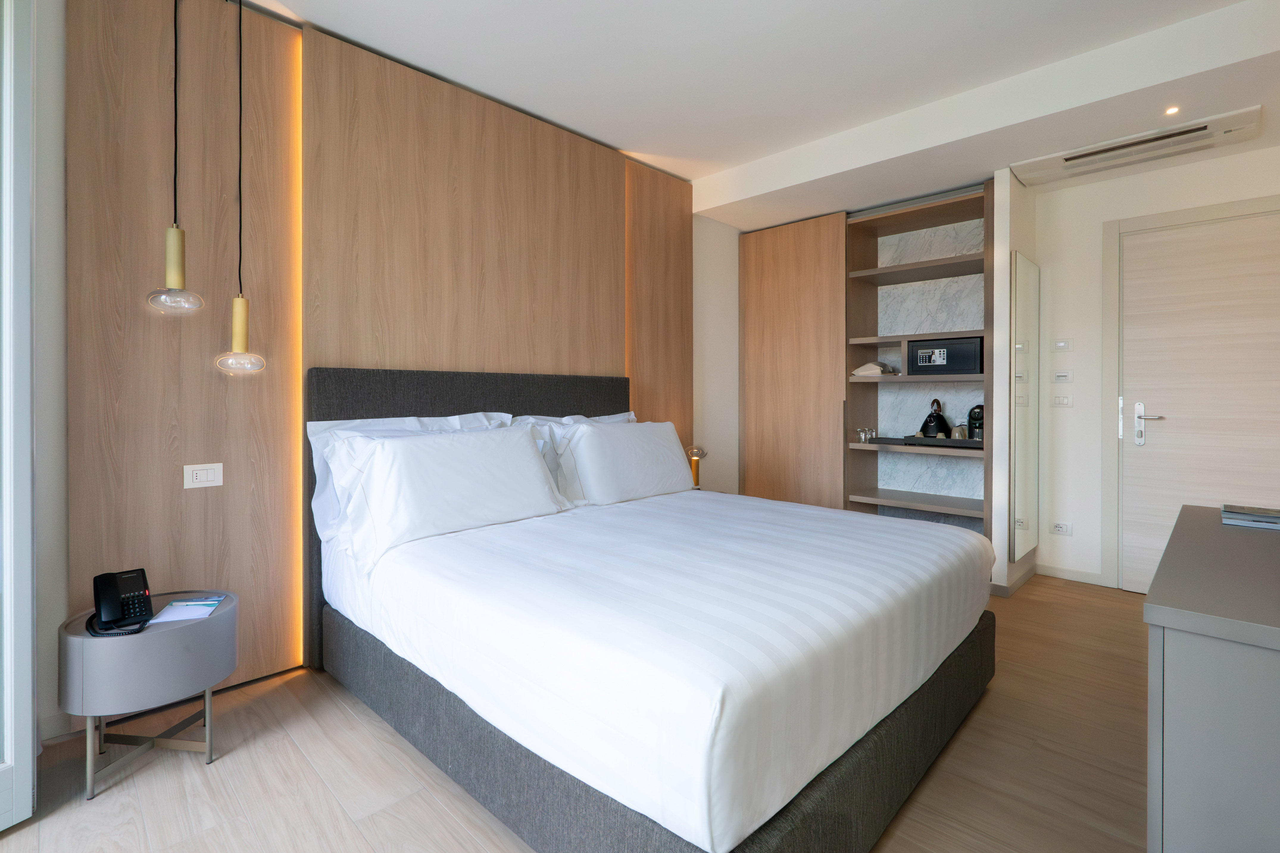 Modern hotel bedroom with queen bed, wood wall, ambient lighting, and built-in storage.