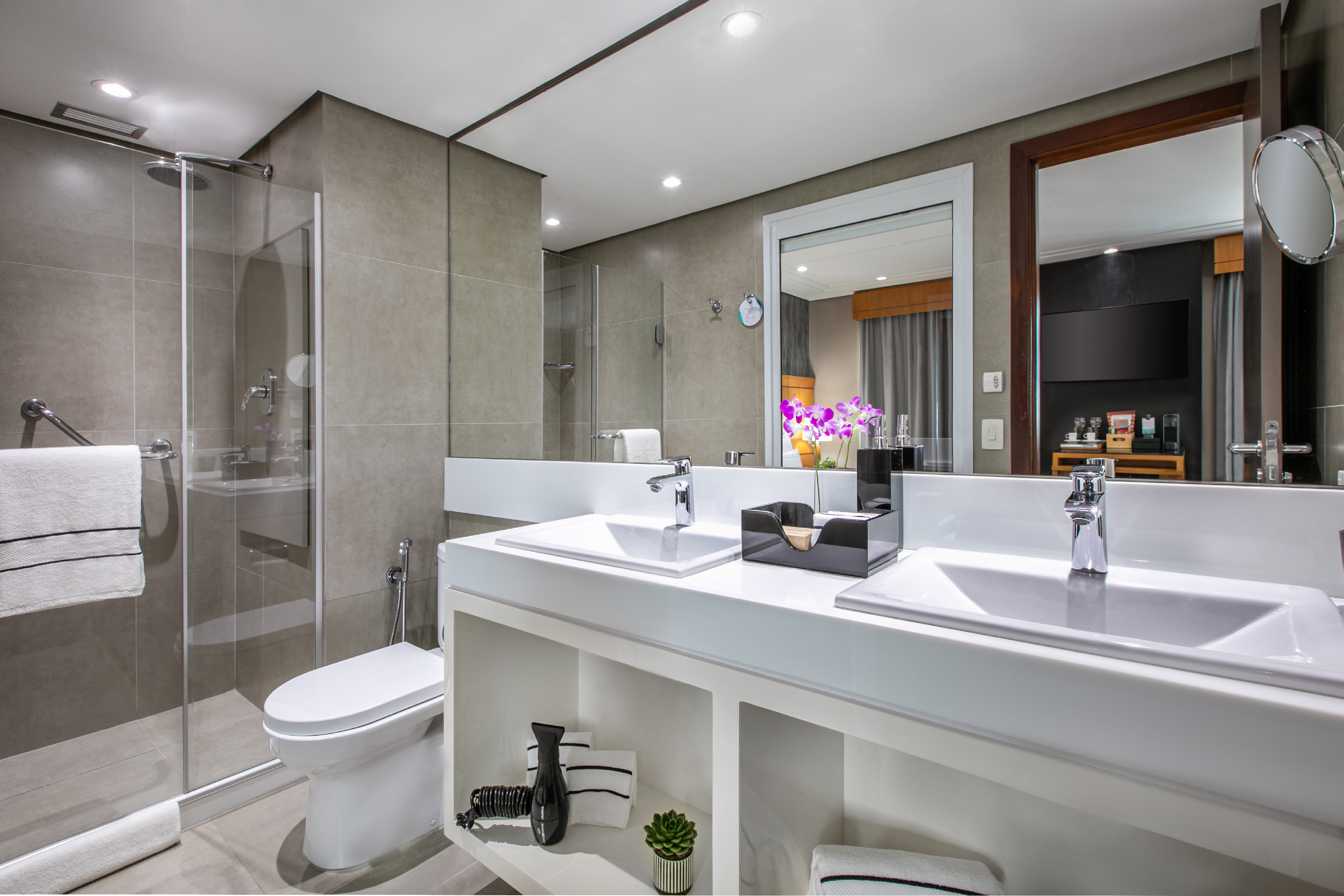 Modern bathroom with glass shower, toilet, white double vanity, and mirror.