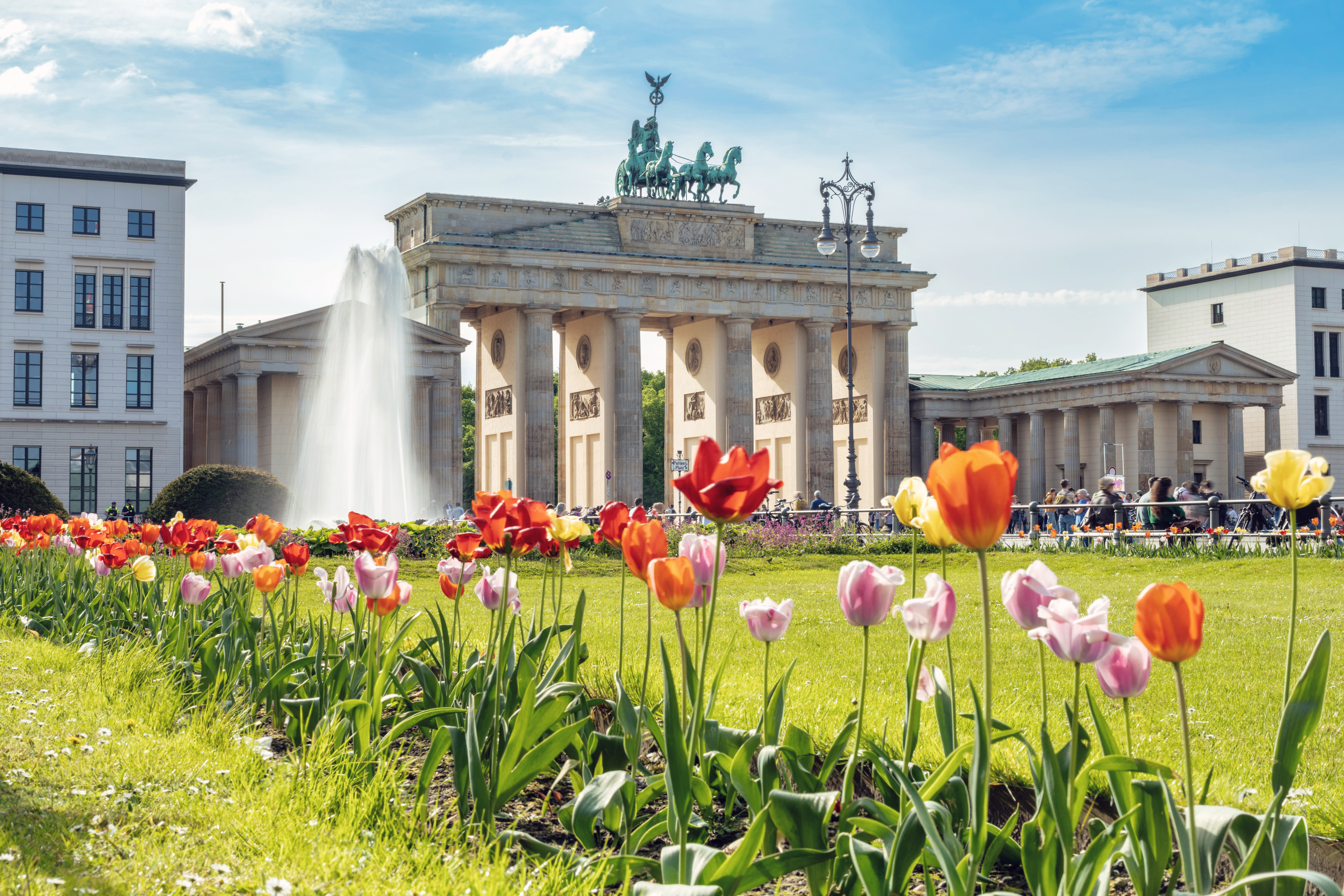 Brandenburg Gate with spring tulips and a fountain in sunny Berlin.