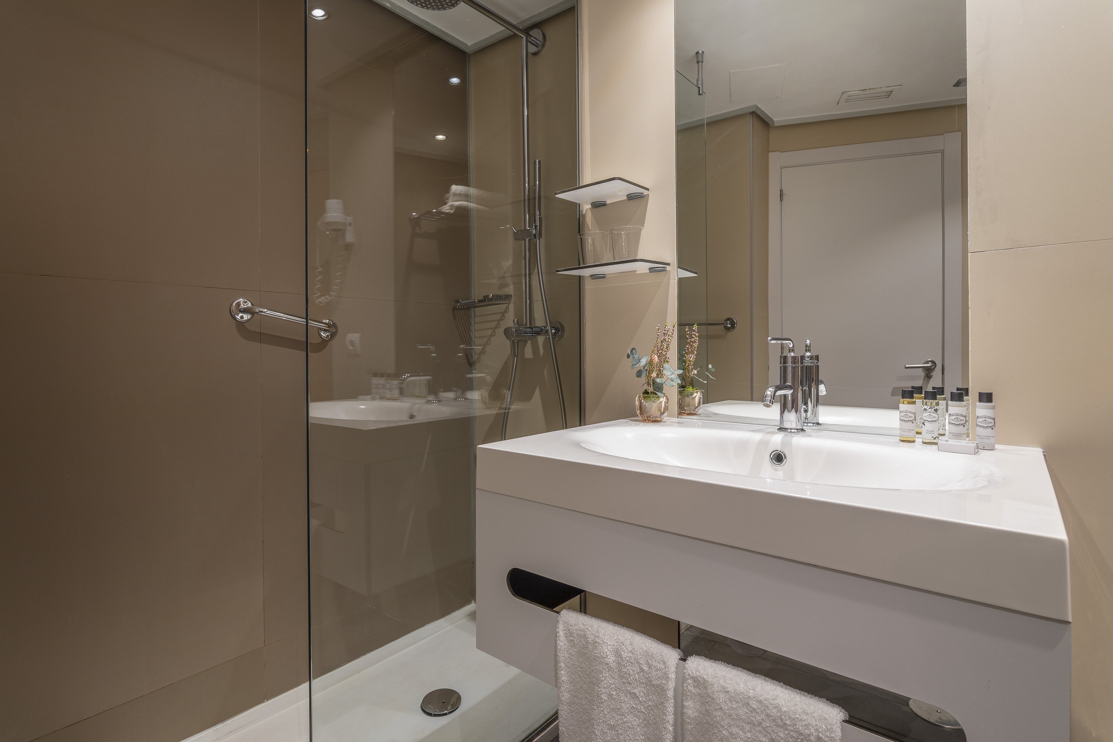 Contemporary hotel bathroom with glass shower and white vanity sink.