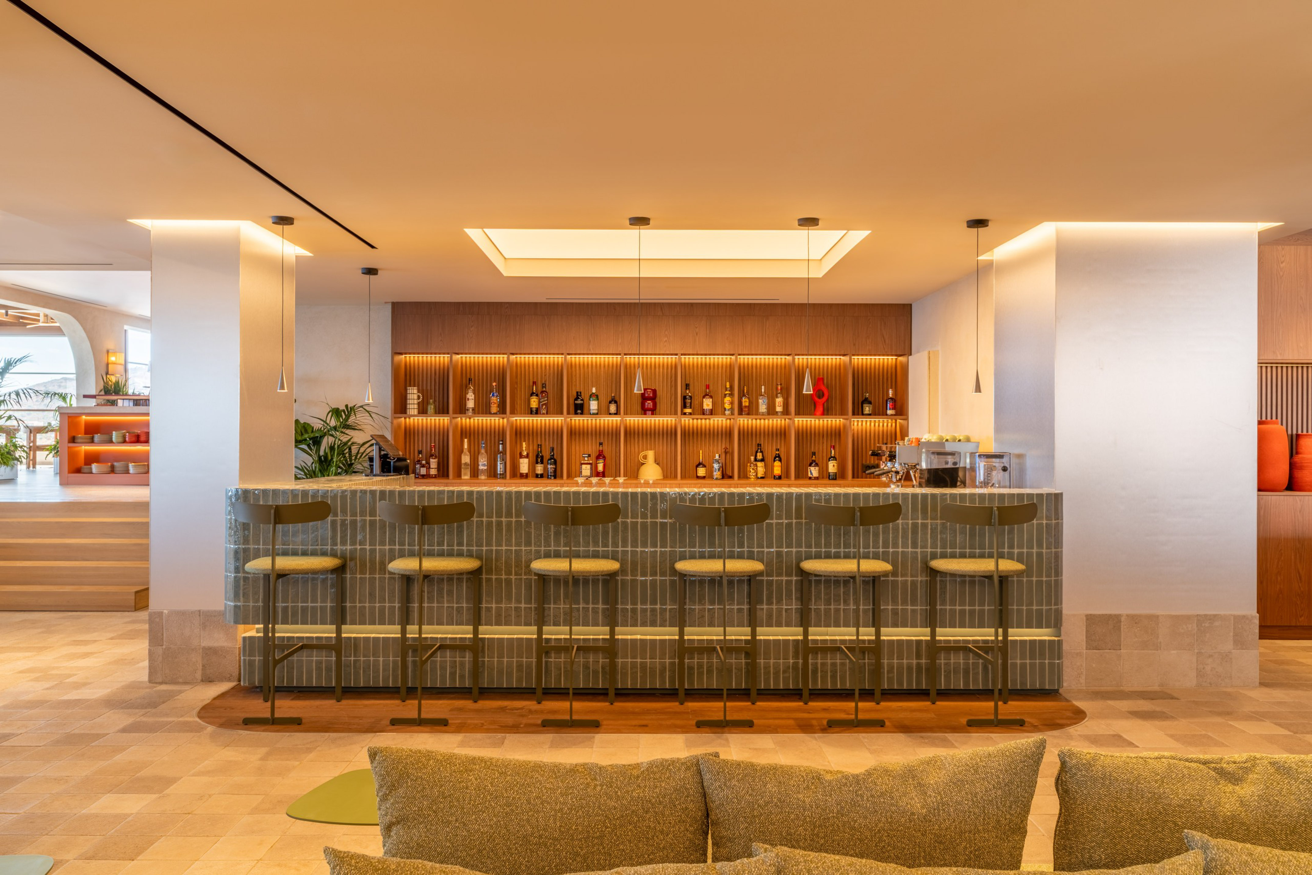 Modern resort bar with tiled counter, bottle display, and ambient lighting.