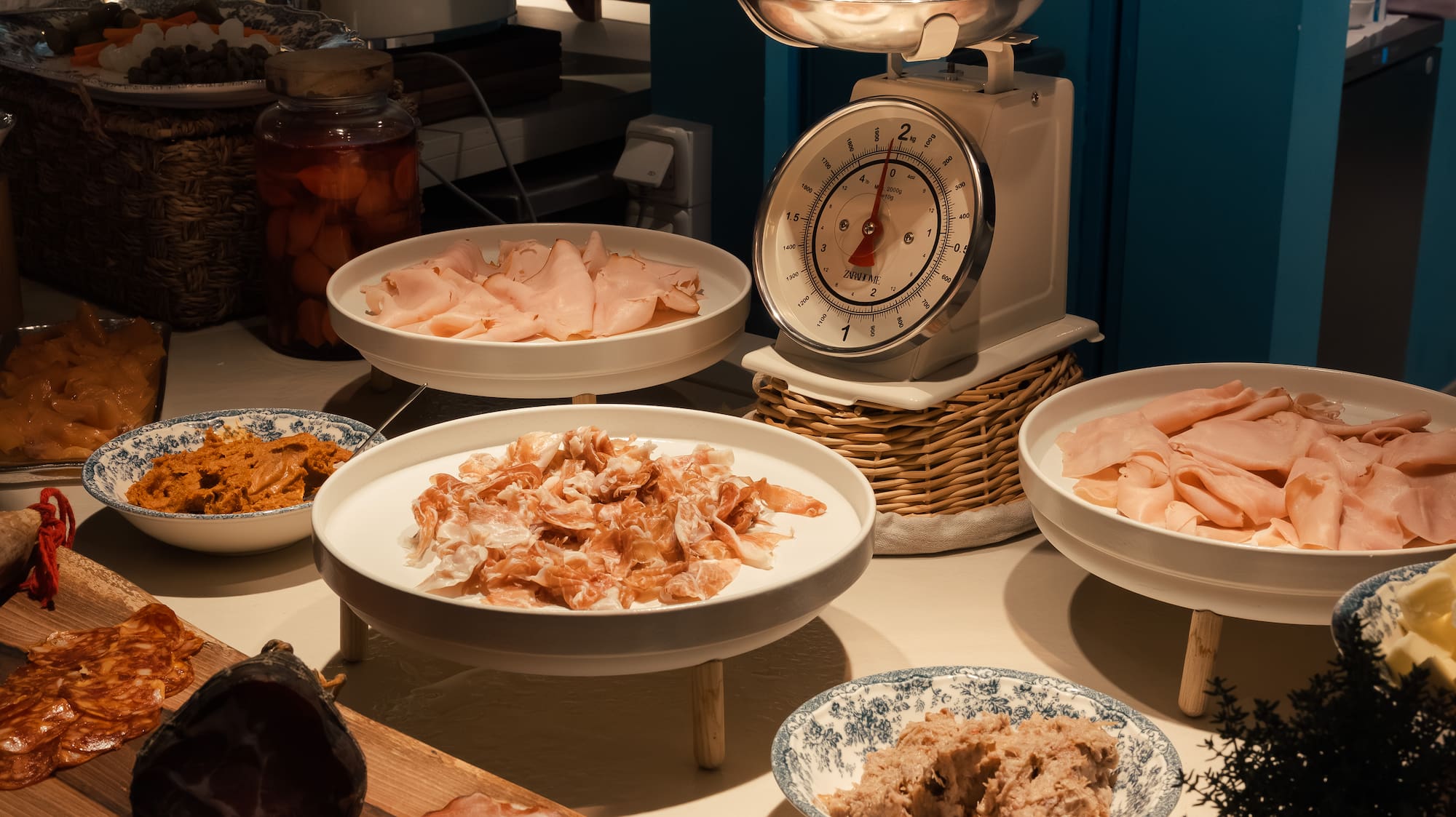 Breakfast buffet with ham, charcuterie, bread, Smeg toaster, and vintage scale.