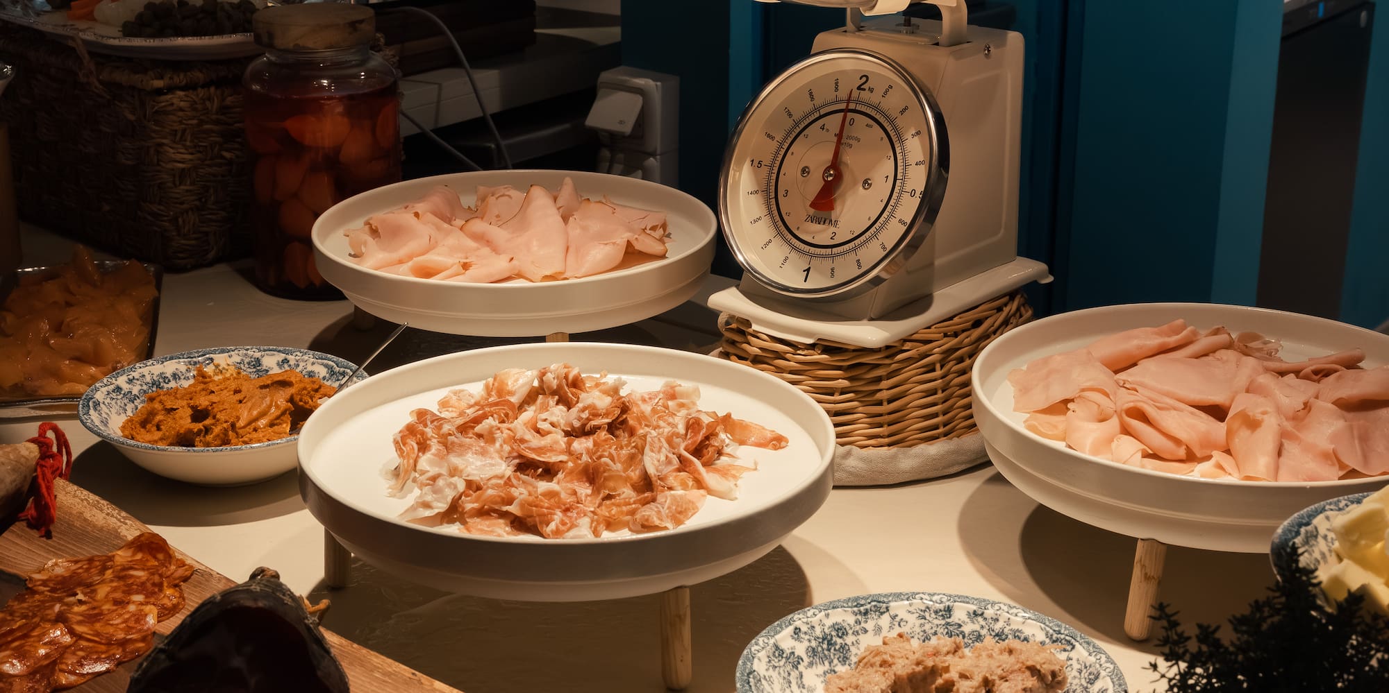 Breakfast buffet with ham, charcuterie, bread, Smeg toaster, and vintage scale.
