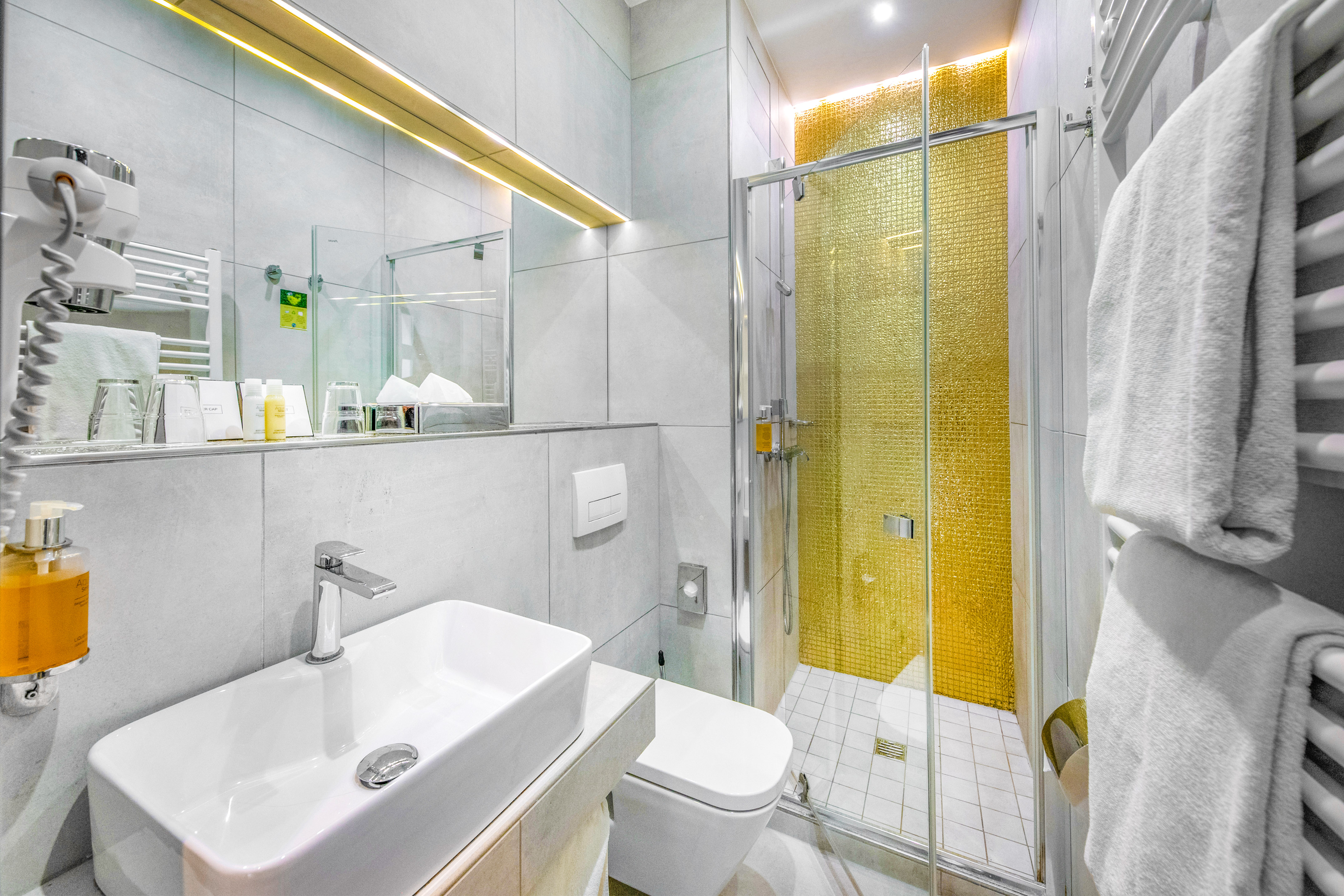 Contemporary hotel bathroom with white basin and gold mosaic shower.