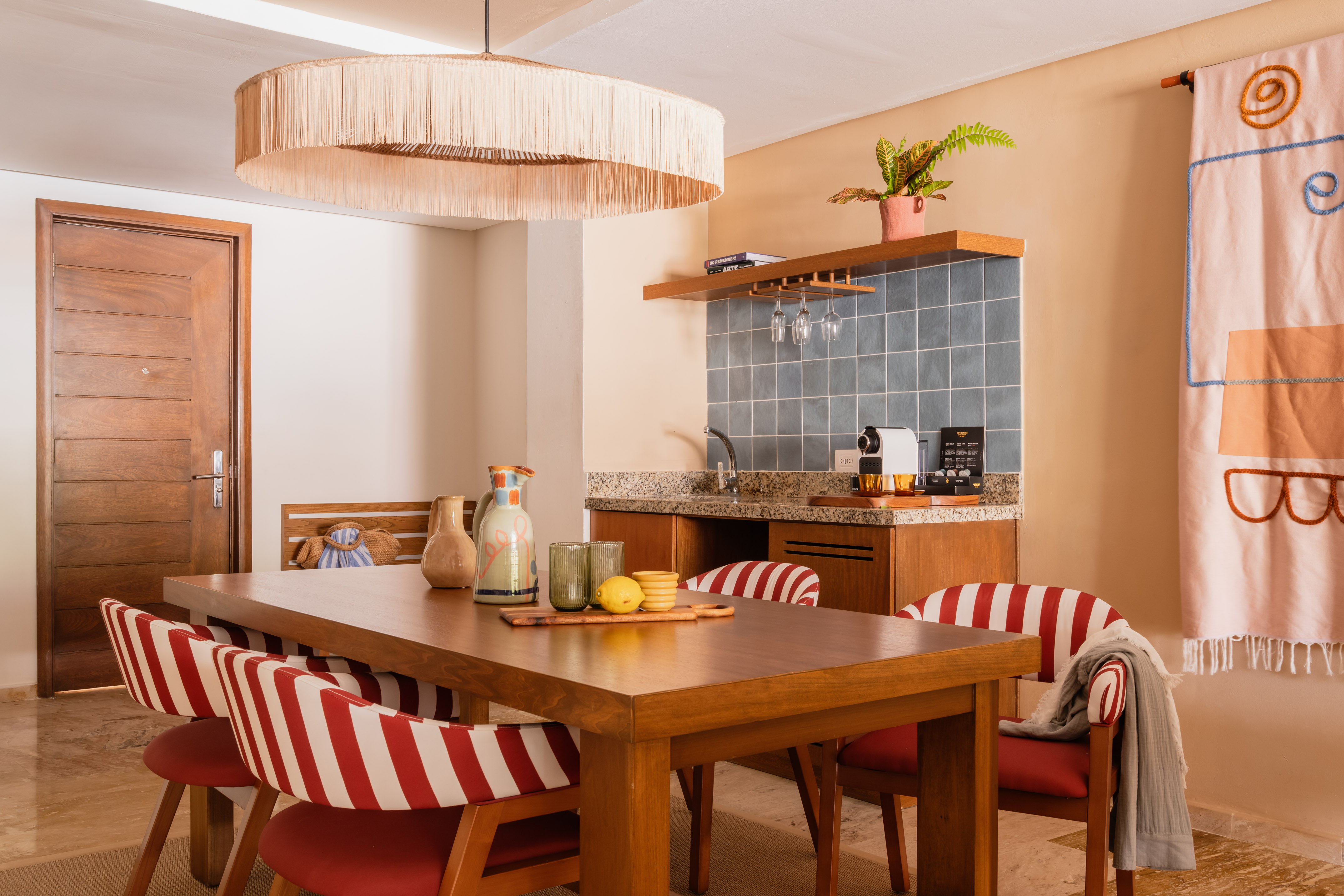 Dining area with wood table, red striped chairs, fringed chandelier, and wet bar.