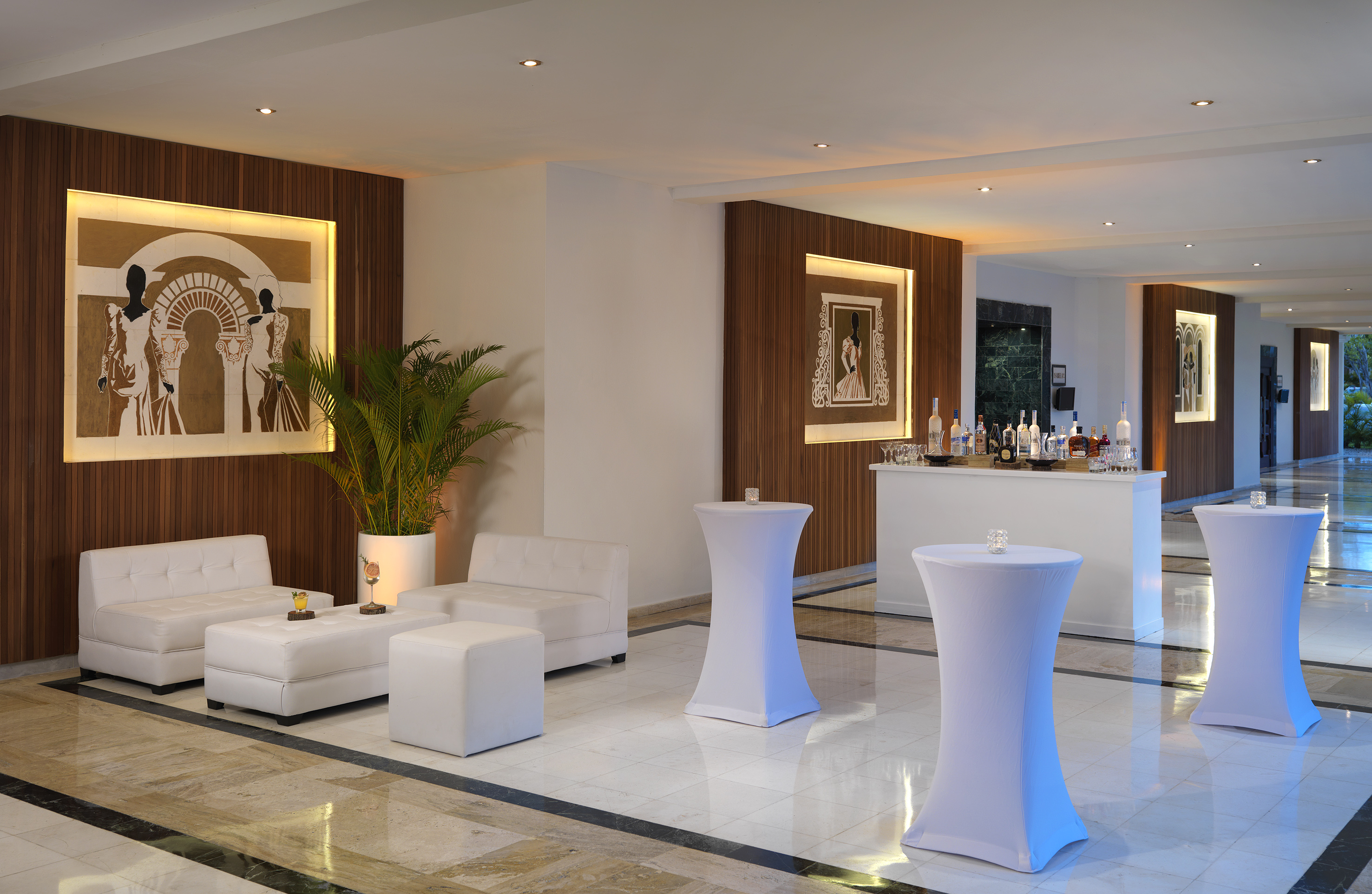 Modern hotel lounge with white seating, a cocktail bar, and high tables.