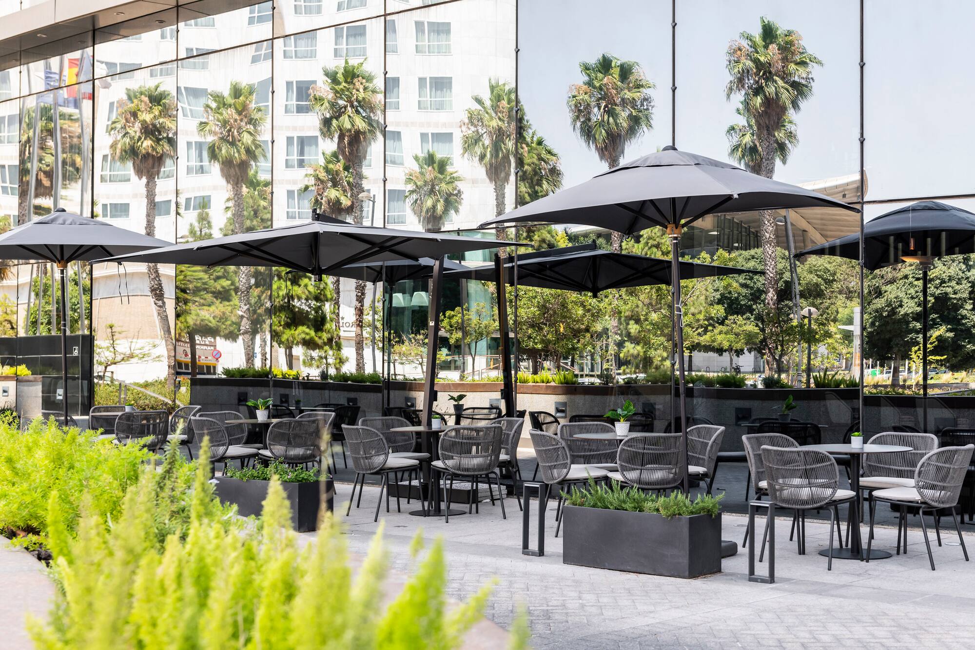 Outdoor dining patio with modern gray chairs, black umbrellas, and glass building.