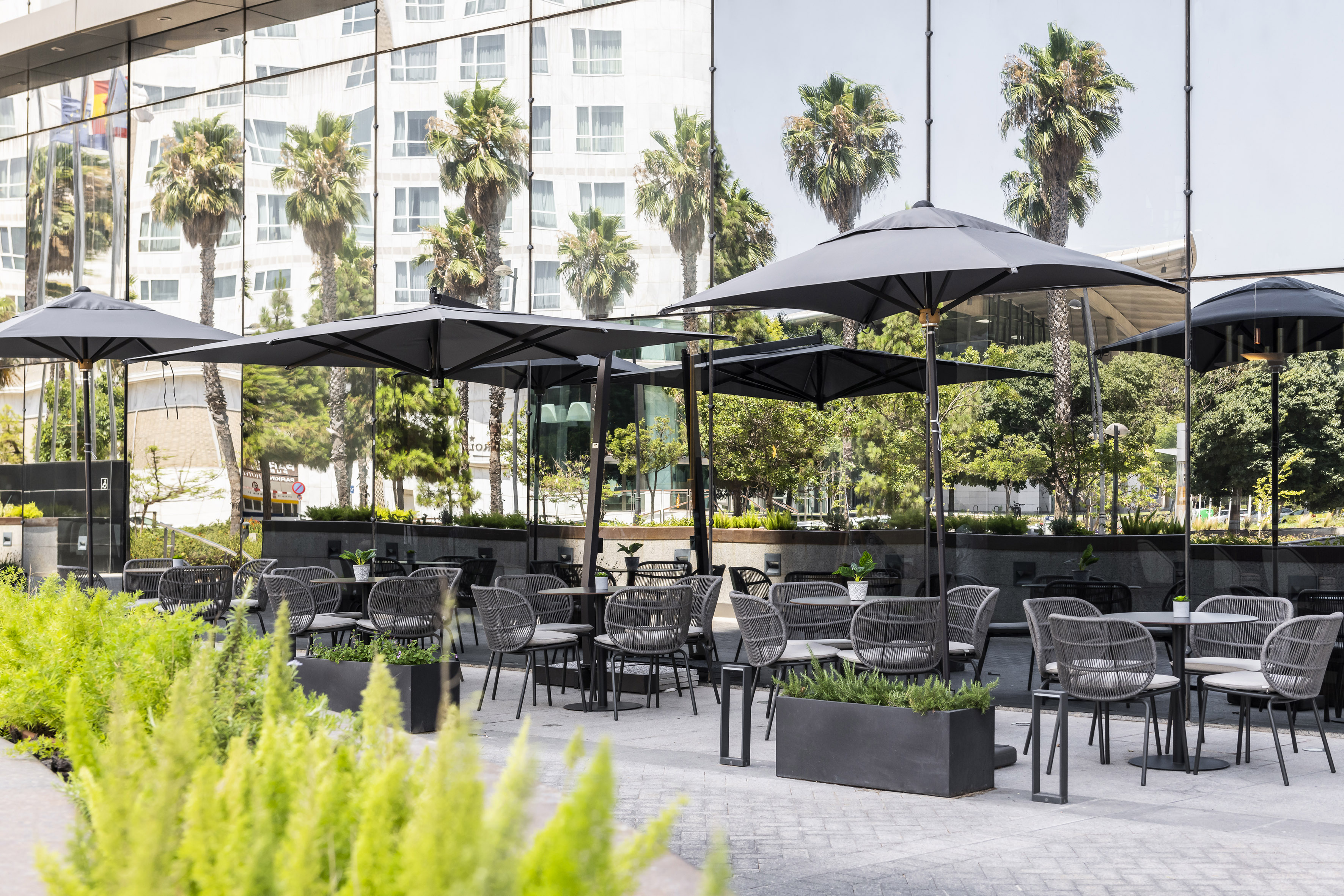 Outdoor dining patio with modern gray chairs, black umbrellas, and glass building.