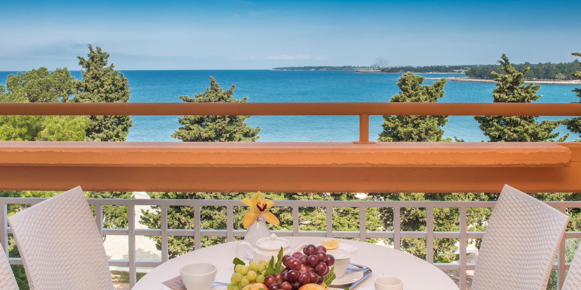 a table with fruit on it and chairs on a balcony overlooking the ocean