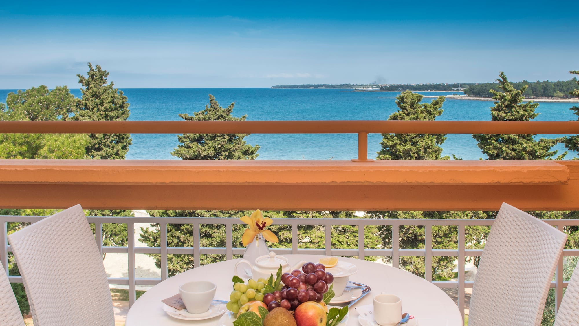 a table with fruit on it and chairs on a balcony overlooking the ocean