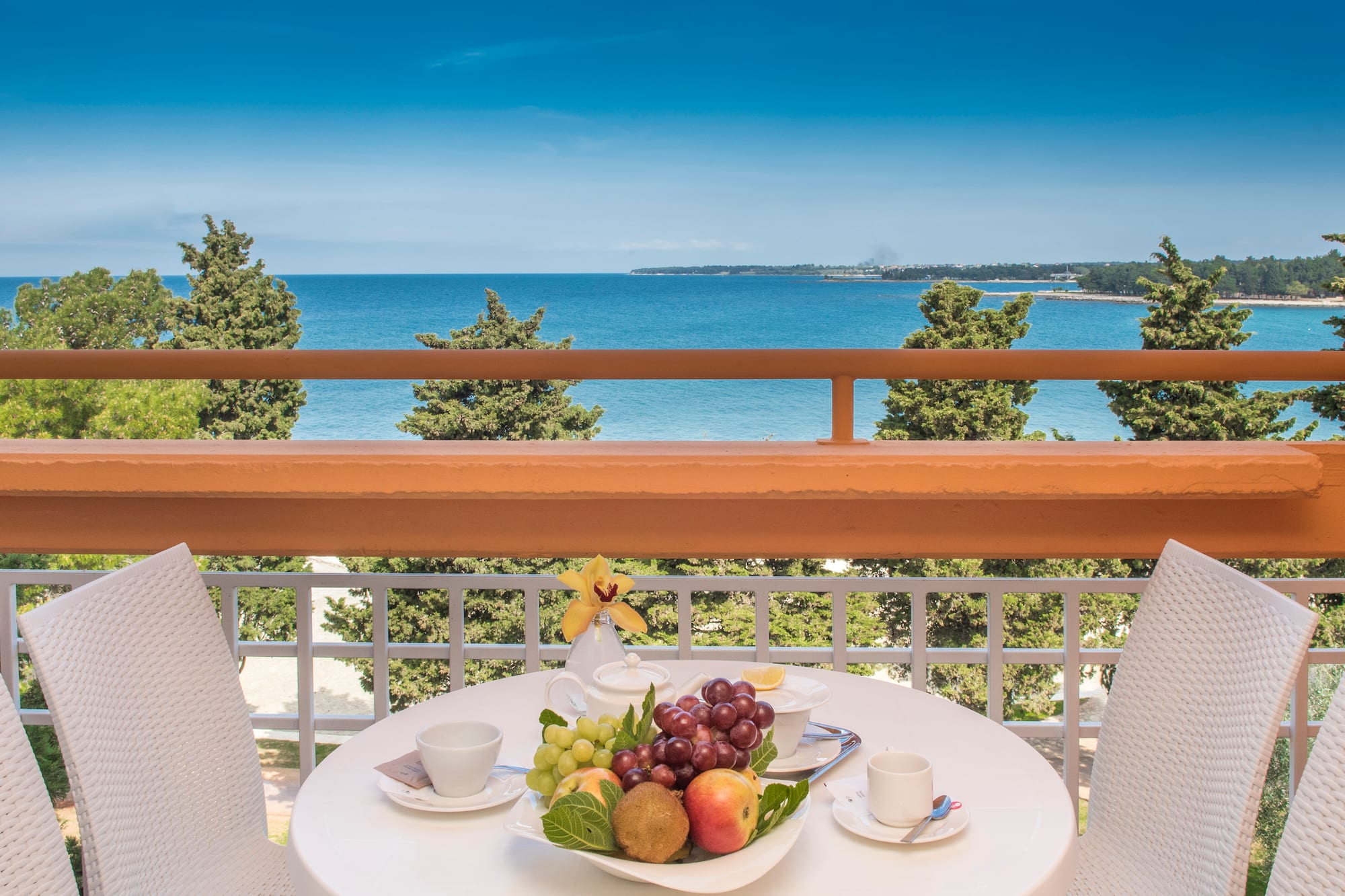 a table with fruit on it and chairs on a balcony overlooking the ocean