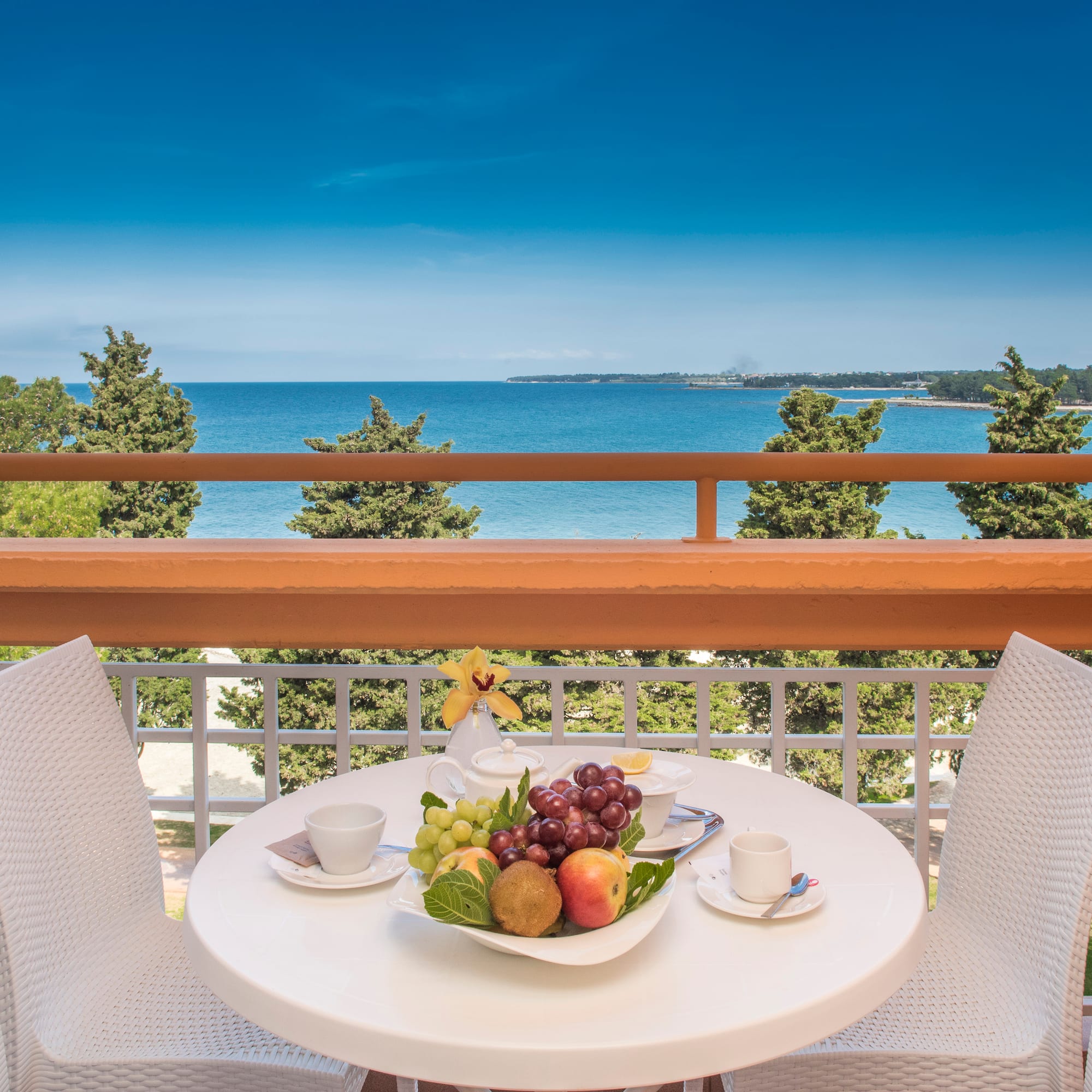 a table with fruit on it and chairs on a balcony overlooking the ocean