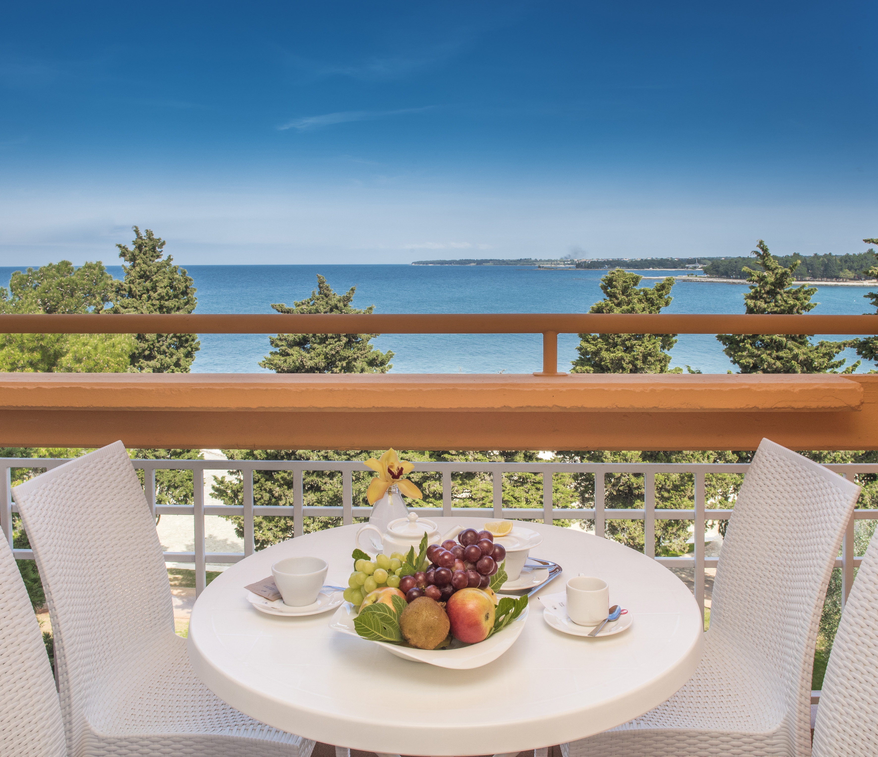 a table with fruit on it and chairs on a balcony overlooking the ocean