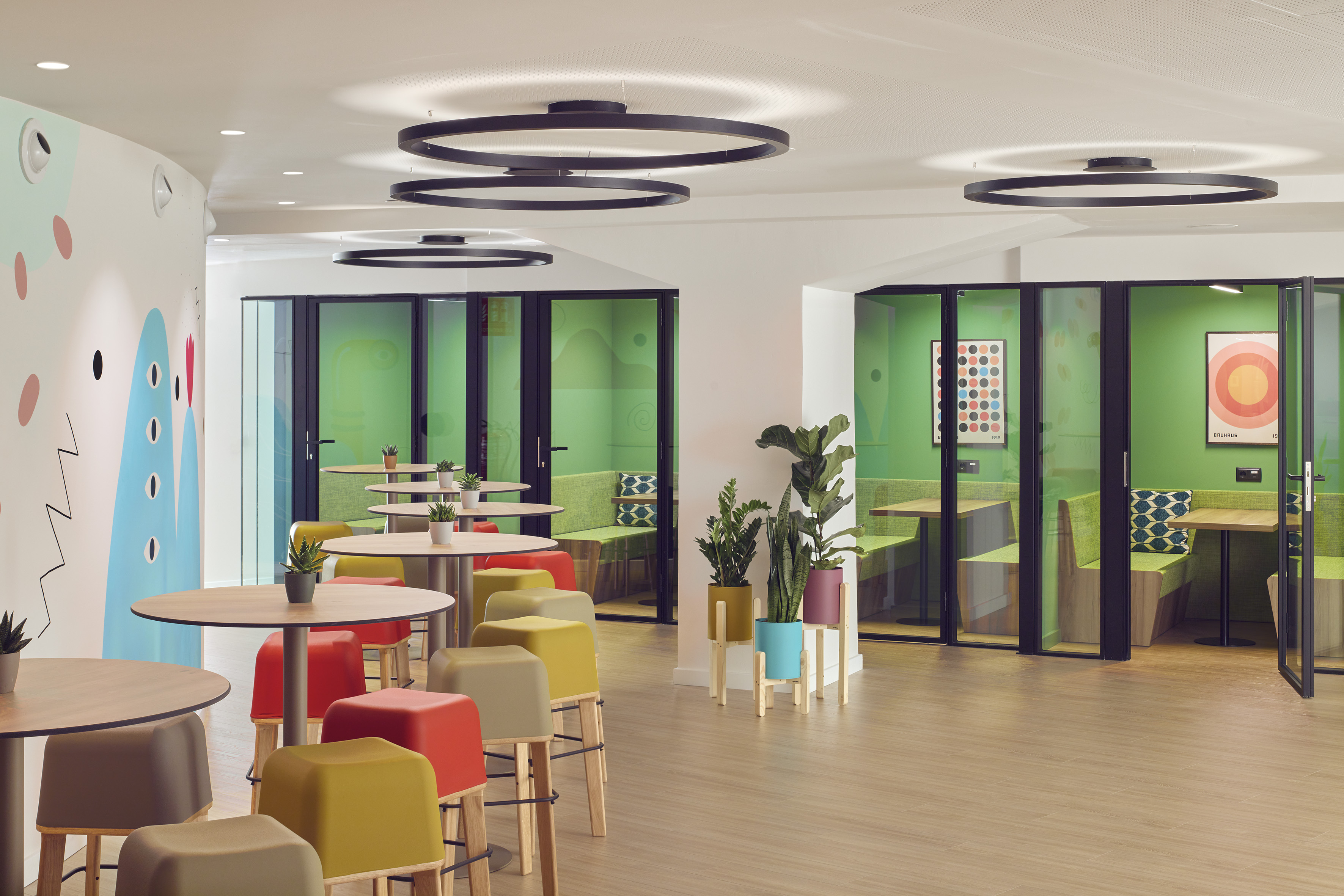 Bright modern office with colorful stools, green meeting pods, and round tables.