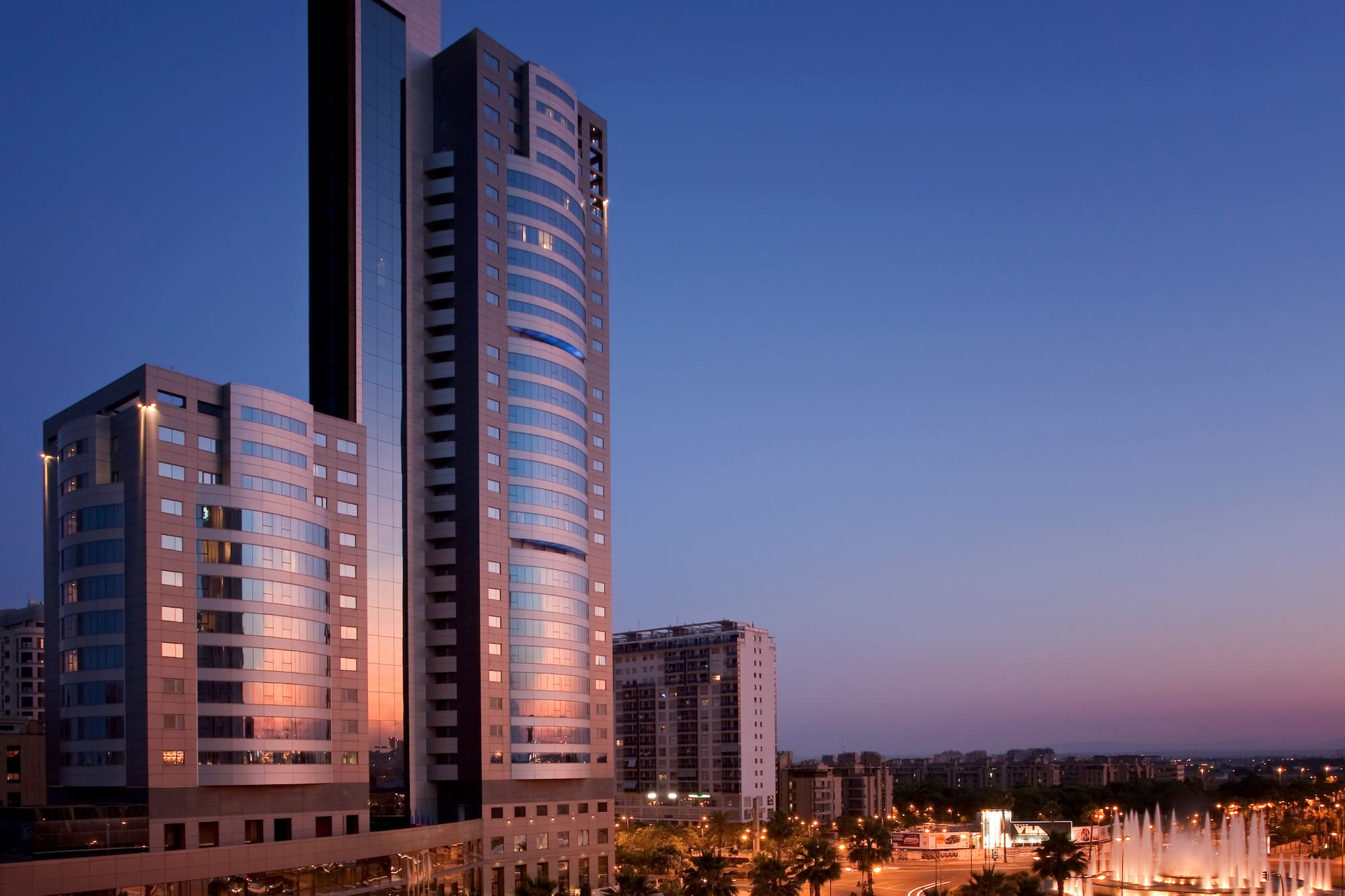 Meliá hotel and city at dusk with illuminated fountain, palm trees.