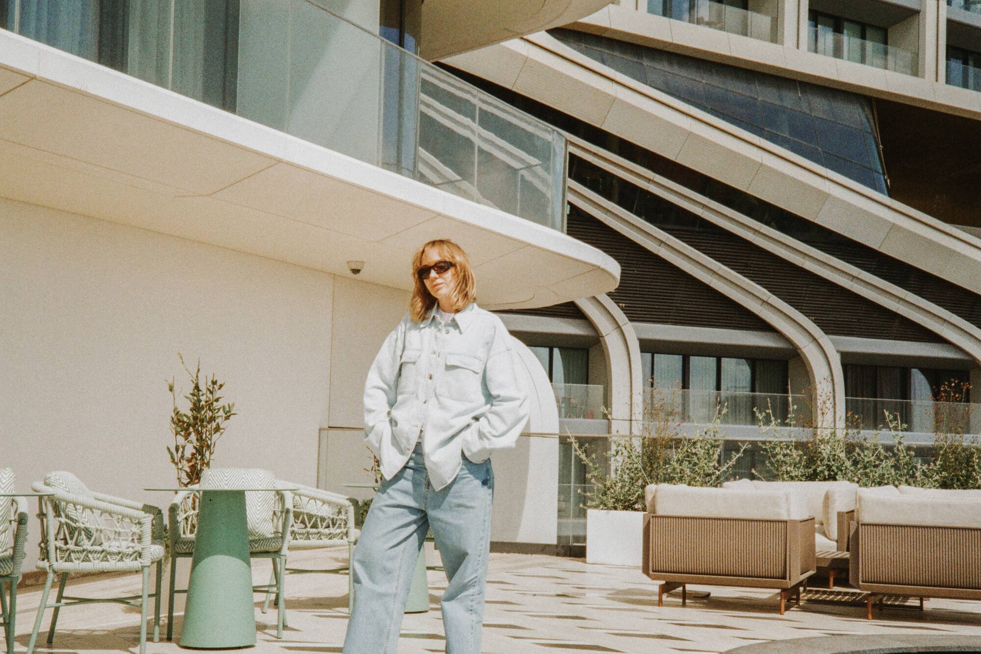 Mujer en vaqueros y camisa denim, terraza moderna con piscina.