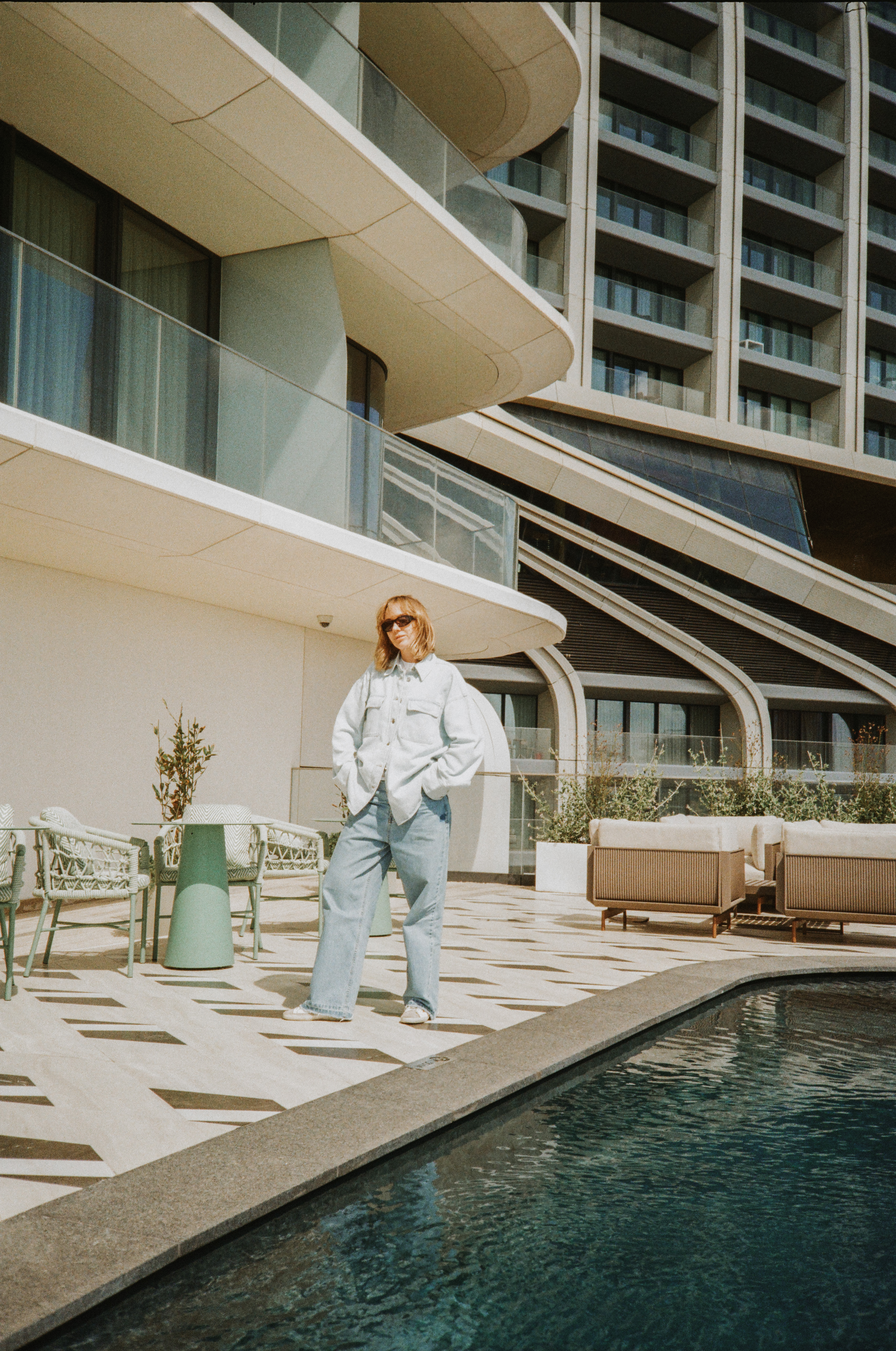 Mujer en vaqueros y camisa denim, terraza moderna con piscina.
