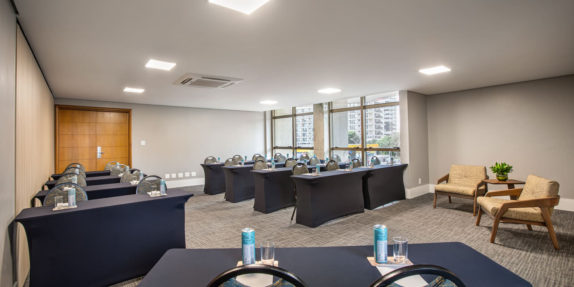 Modern conference room with rows of tables, chairs, lounge area, and city view.