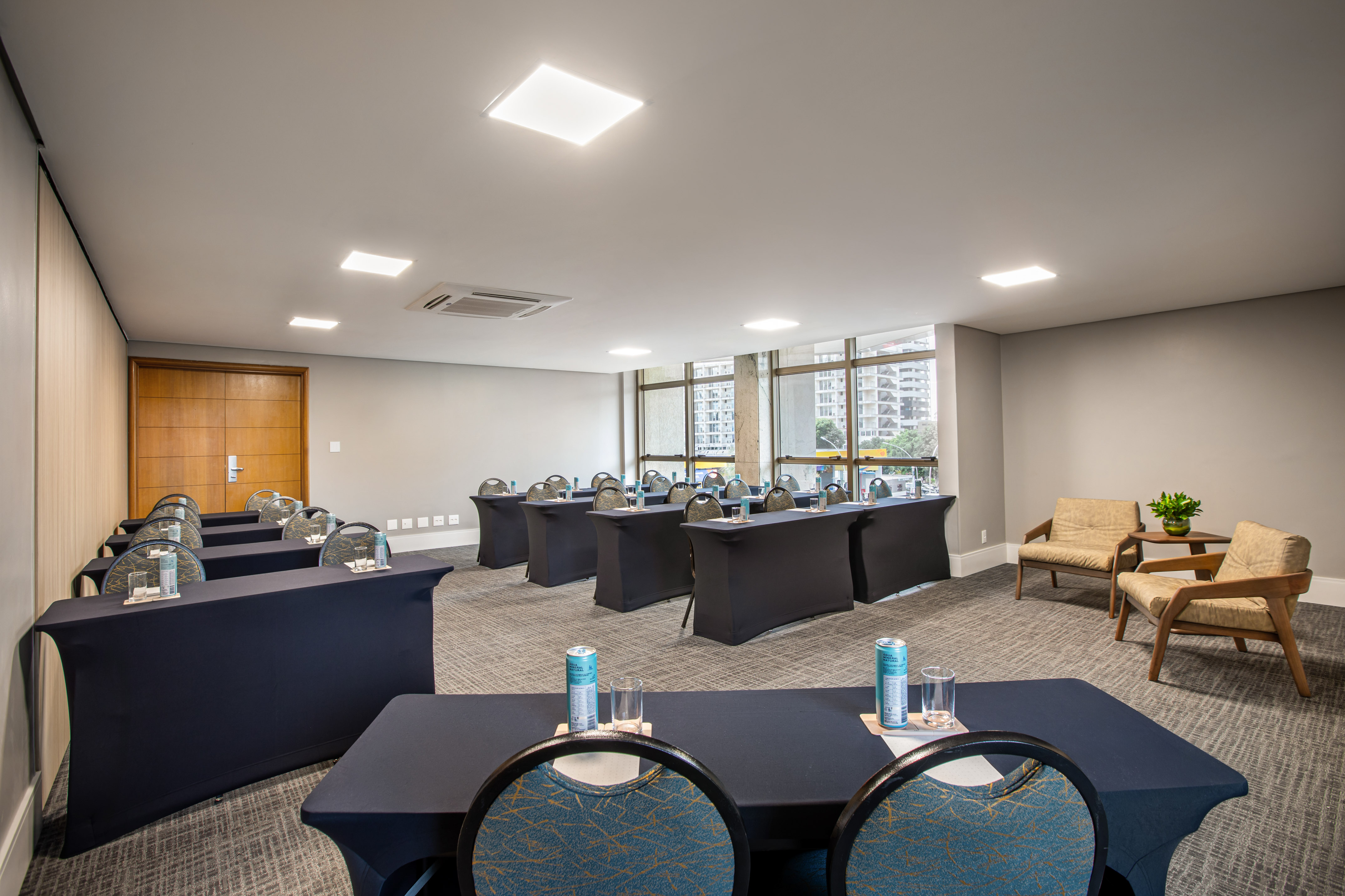 Modern conference room with rows of tables, chairs, lounge area, and city view.