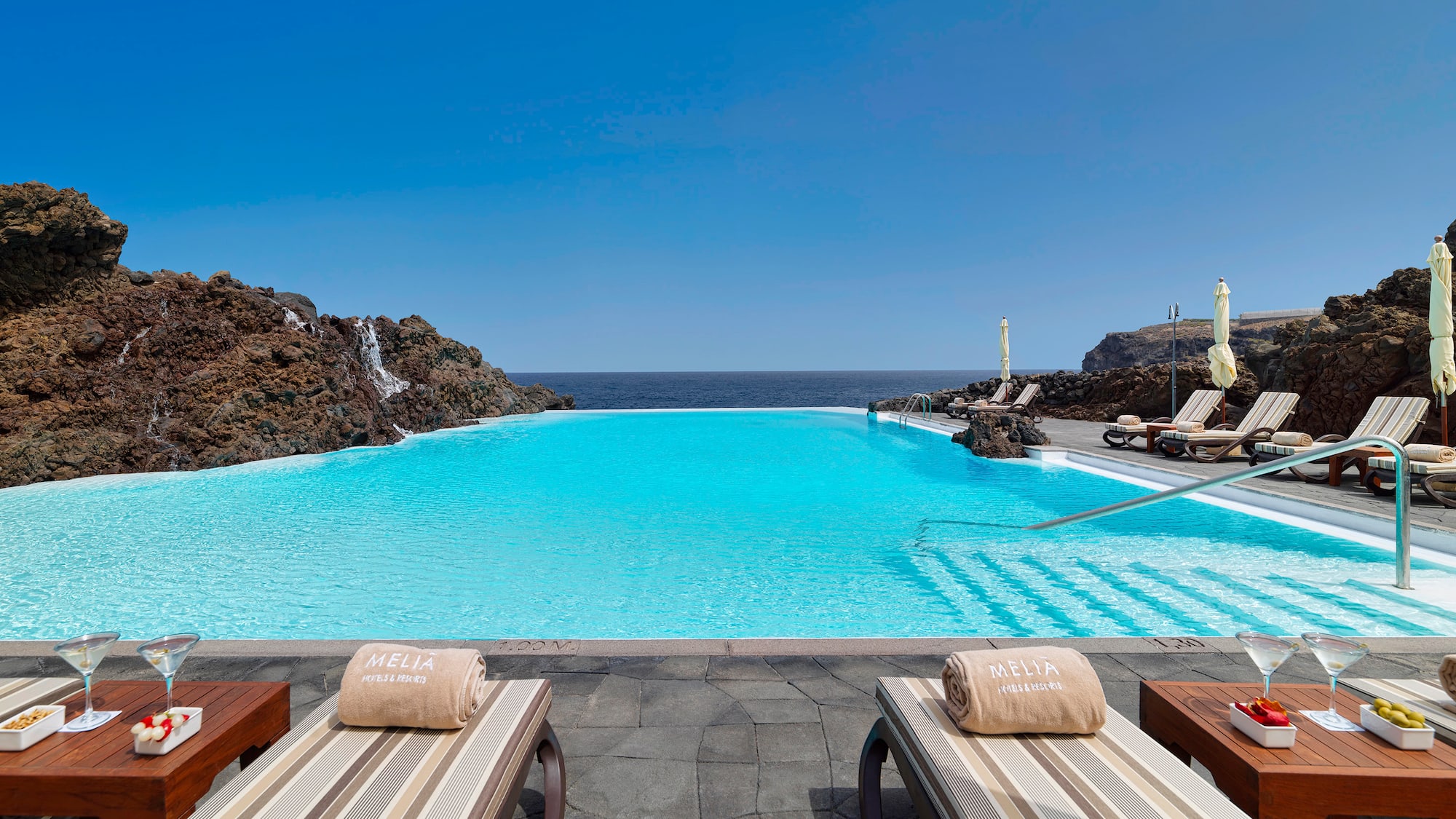 Meliá infinity pool with ocean view, rocky coast, and sun loungers.