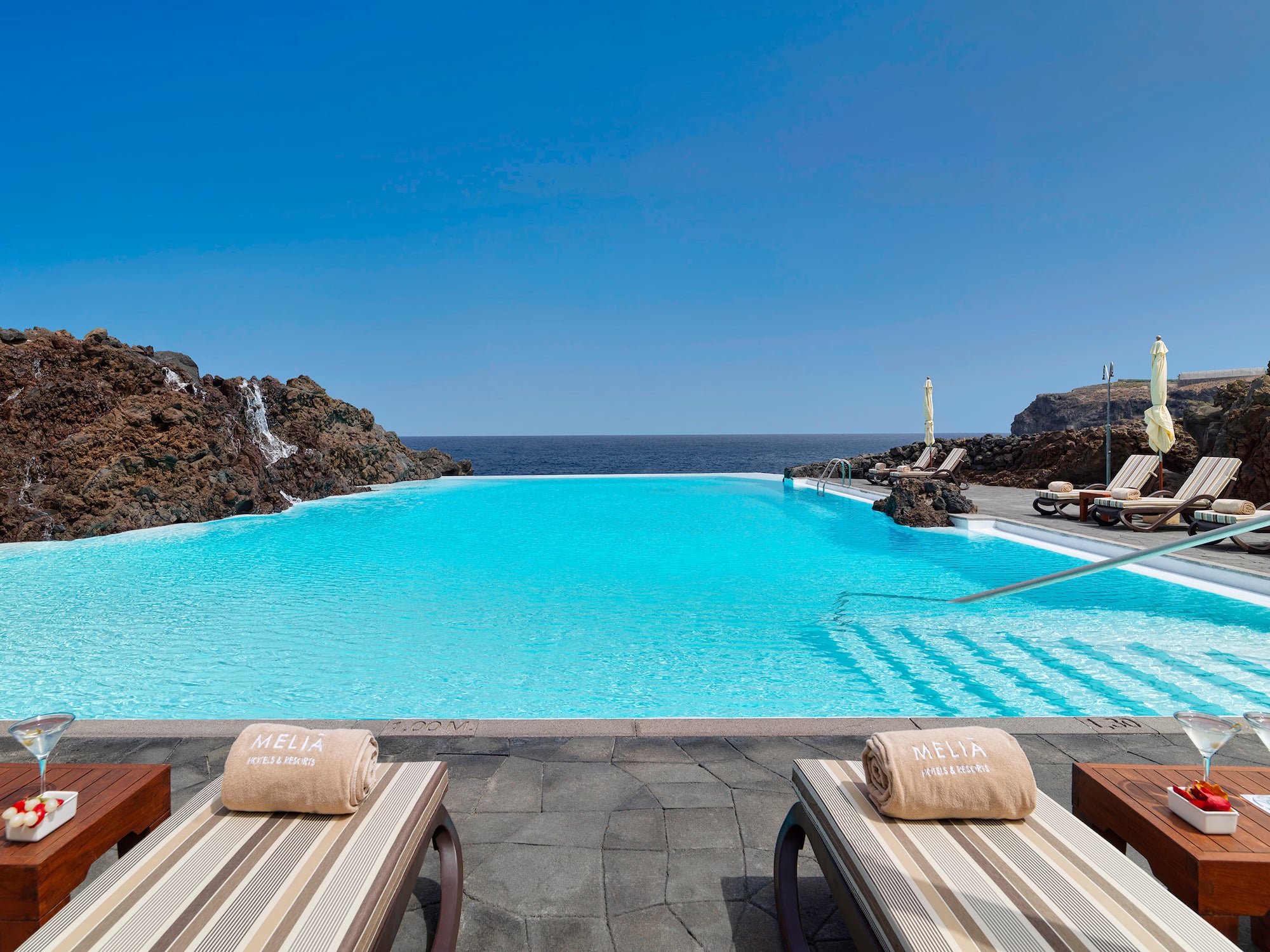 Meliá resort infinity pool with ocean view, lounge chairs, and cocktails.