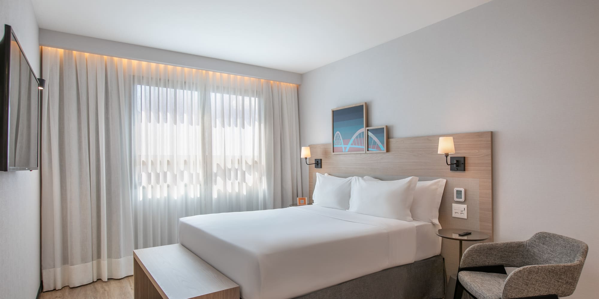 Bright modern hotel room with queen bed, wood headboard, and large window.