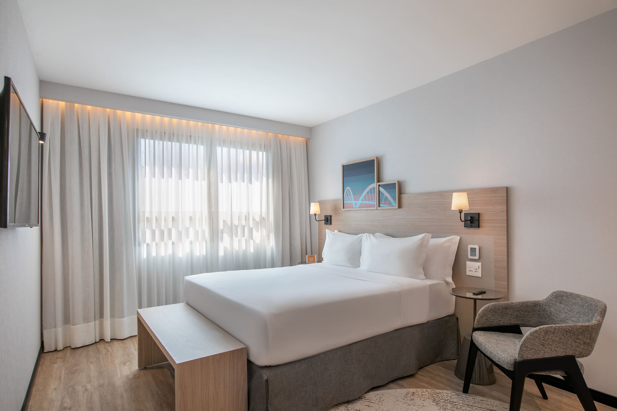 Bright modern hotel room with queen bed, wood headboard, and large window.