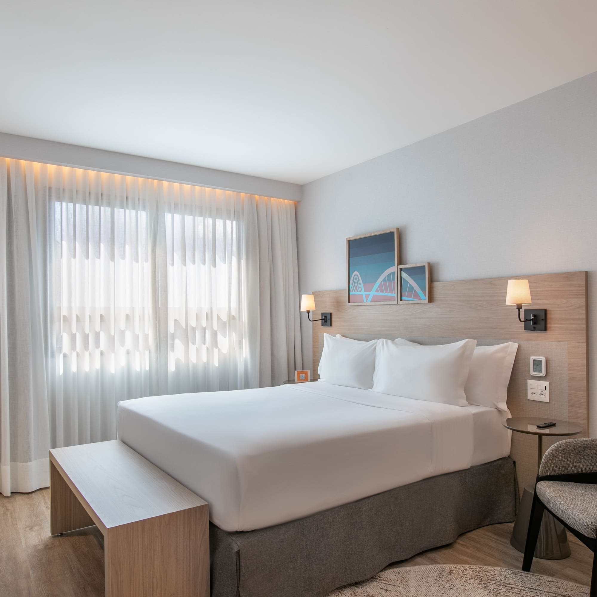 Bright modern hotel room with queen bed, wood headboard, and large window.