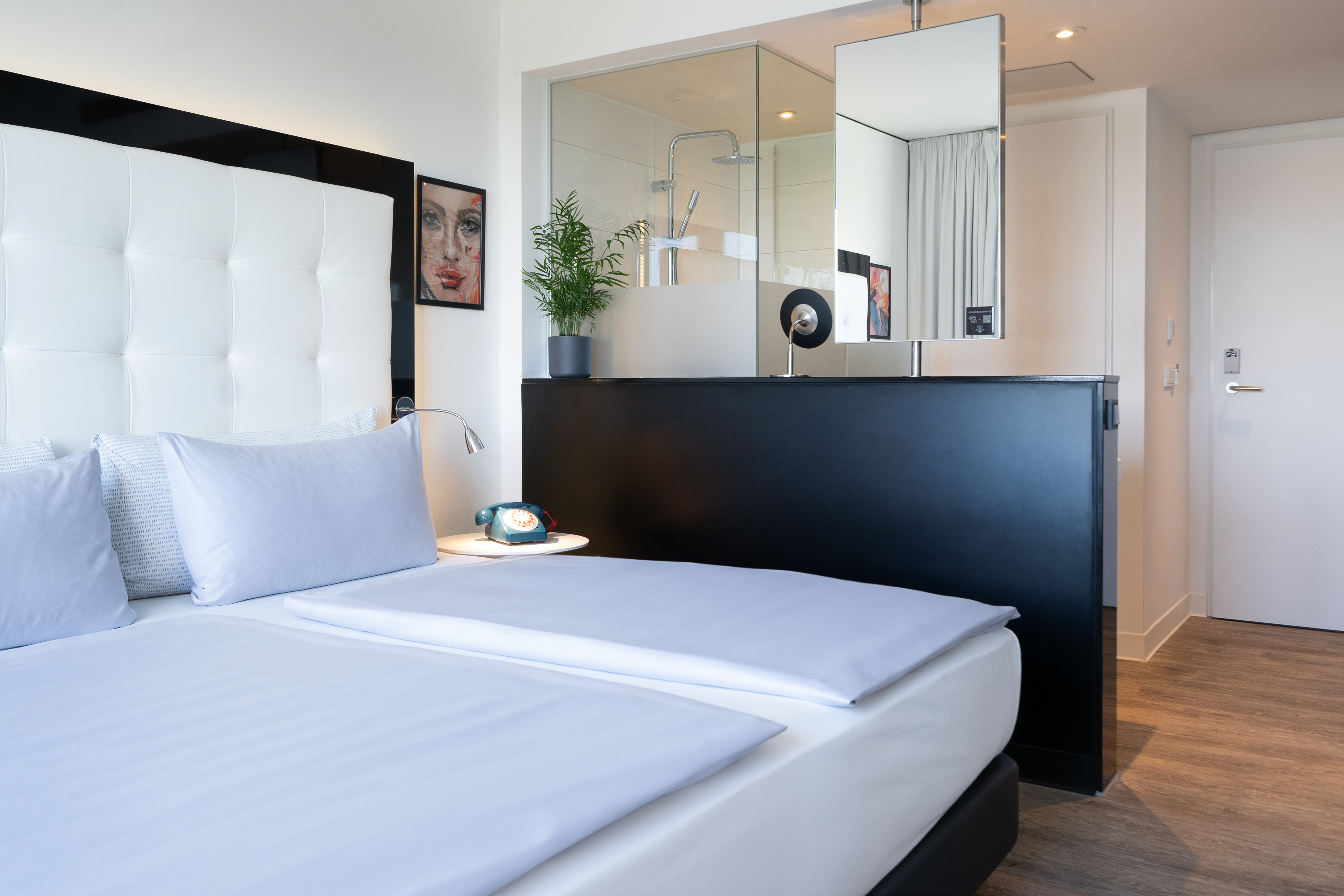 Modern hotel room with bed, white headboard, and open glass shower.